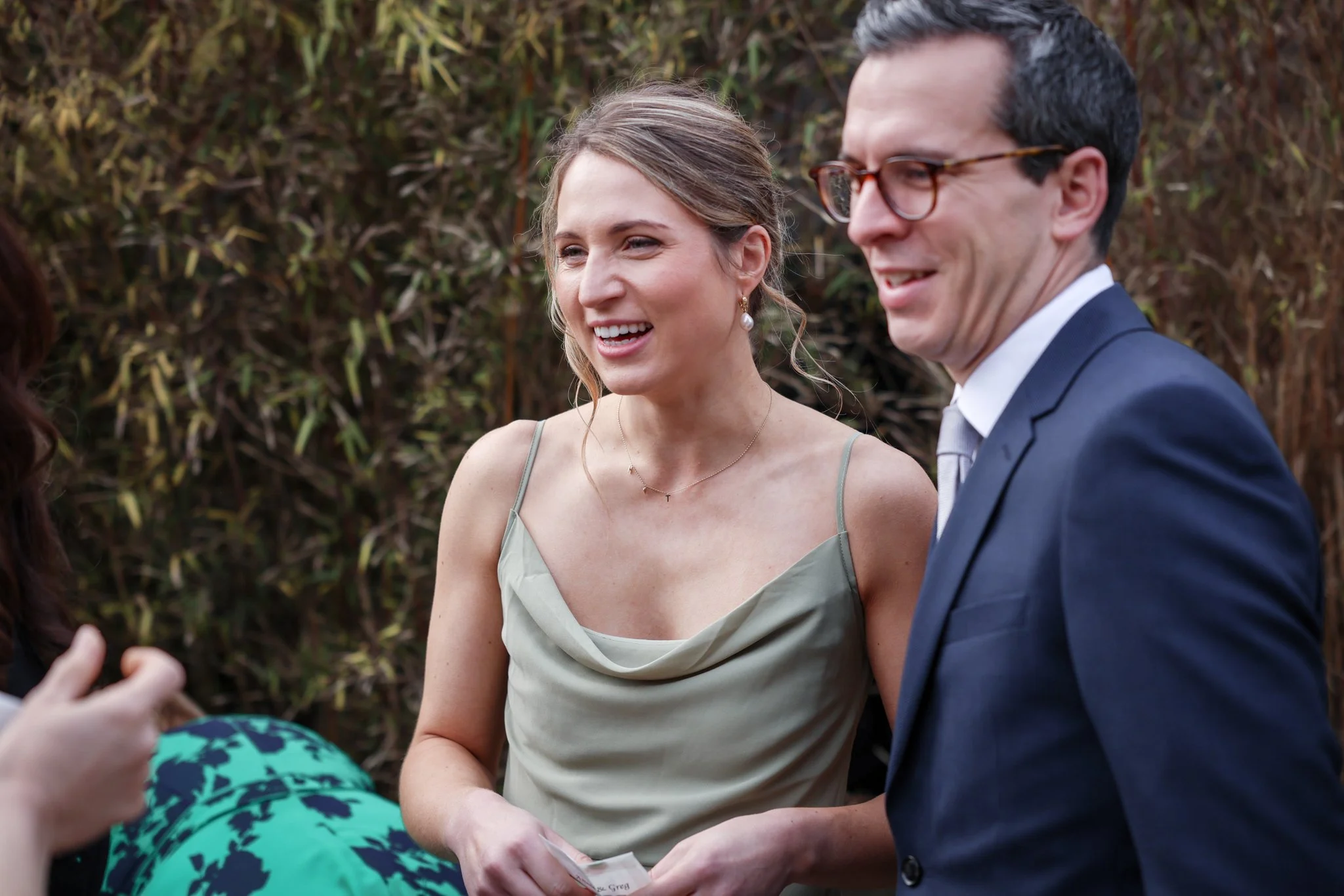 Two smiling women and a man engaged in conversation outdoors with a leafy background.