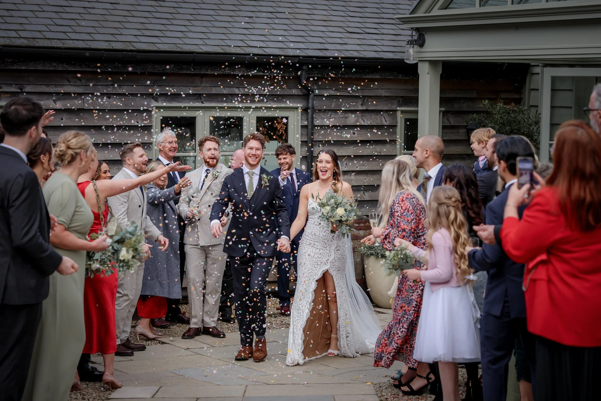 Smiling bride and groom walking through guests during their wedding celebration, with confetti falling around them