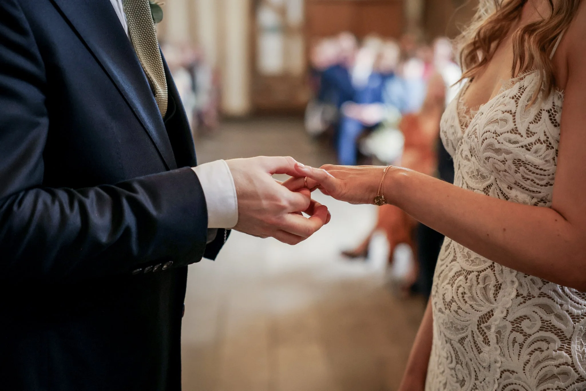 Couple exchanging rings during a wedding ceremony, with guests in the background.