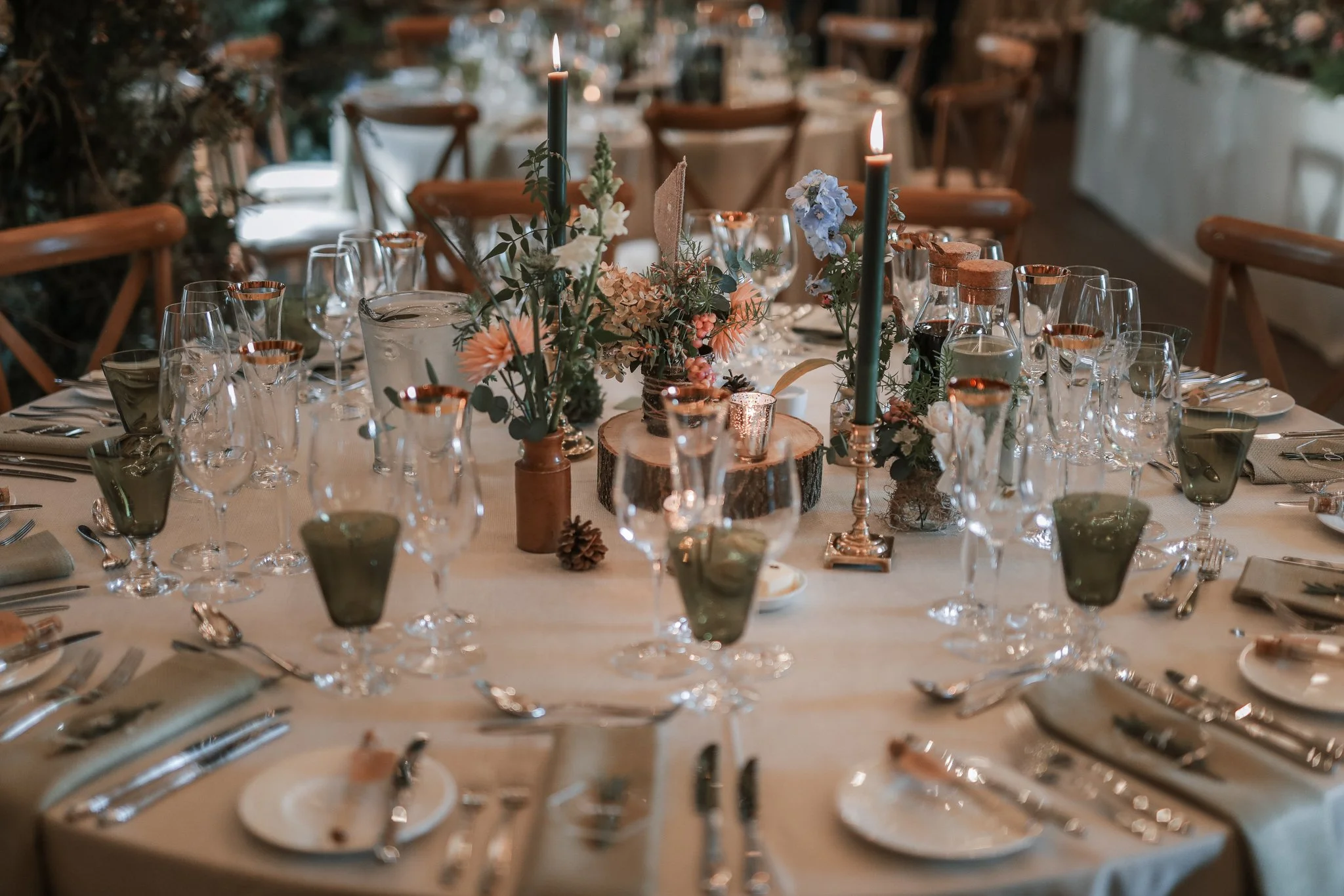 A decorated banquet table with floral centerpieces, candles, and glassware, set for a formal event in a warmly lit indoor space.