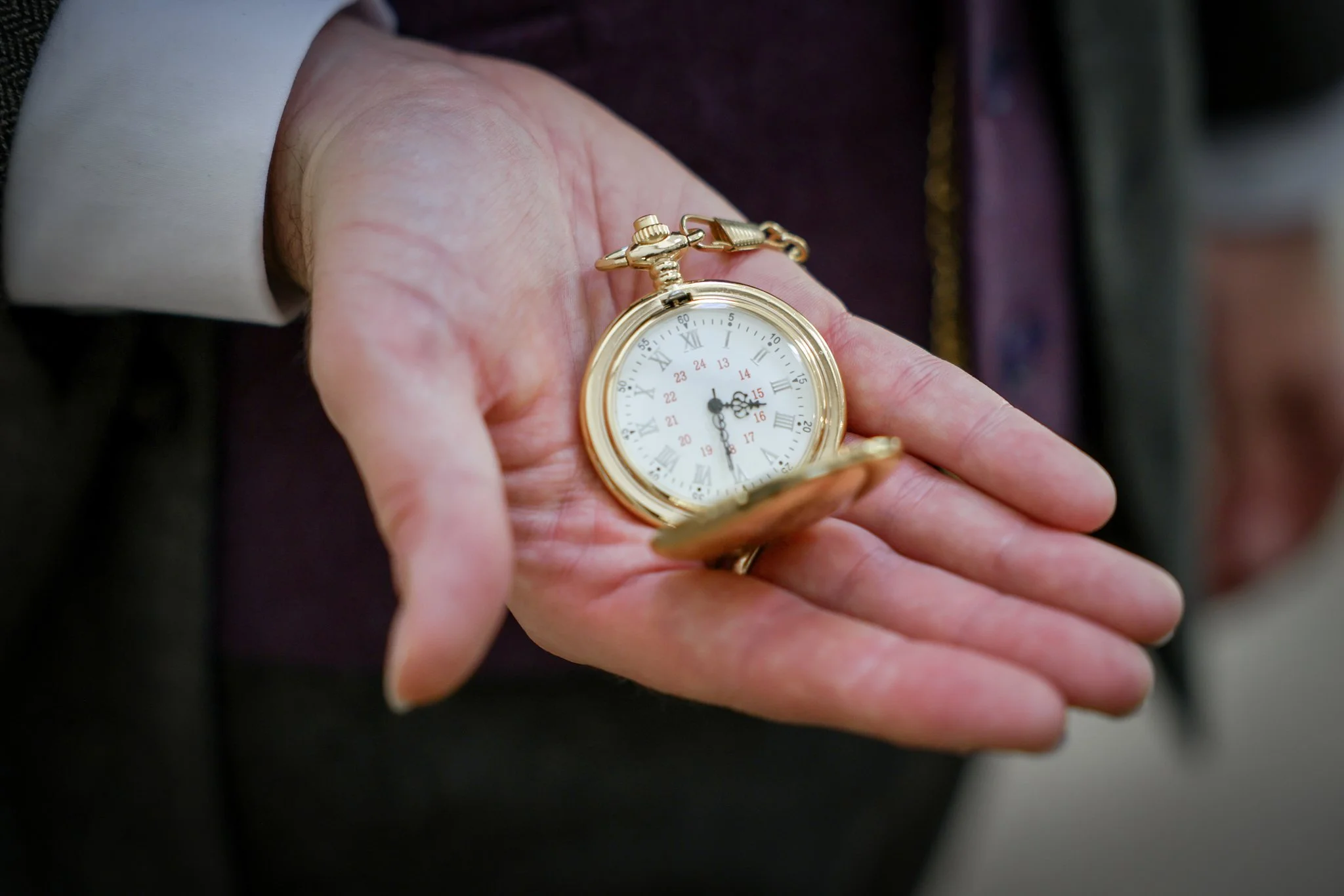 A person holding a gold pocket watch with Roman numerals and a white face.