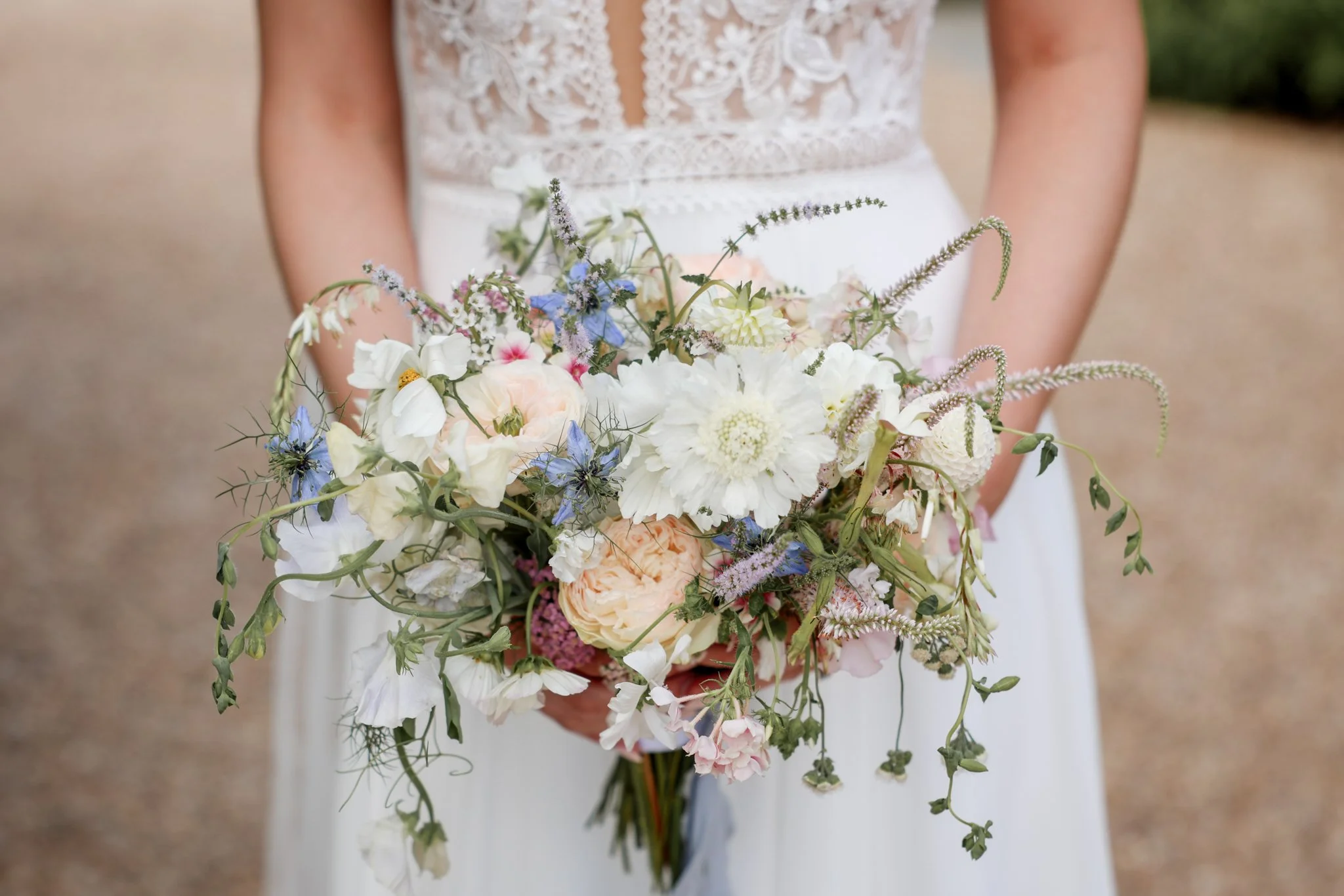 Close-up of a bride holding a colorful bouquet of various flowers including white, peach, pink, purple, and blue blossoms.