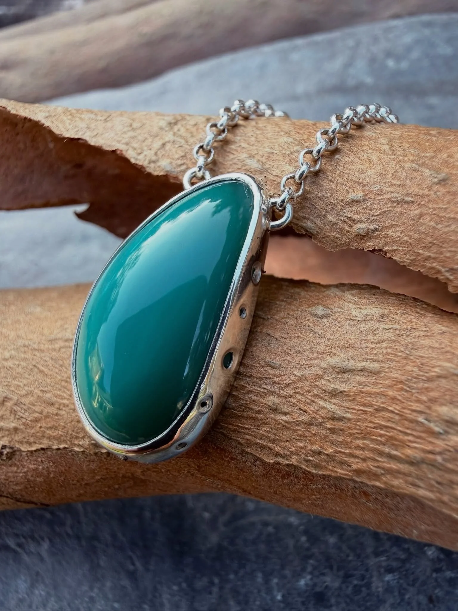 An unusual pendant. Teardrop teal opalised wood from Indonesia set in sterling silver with open back &amp; pierced sides. The silver chain is adjustable to 16&rdquo;, 17&rdquo; and 18&rdquo; with an easy open jump ring &amp; a dinky chain charm. Avai