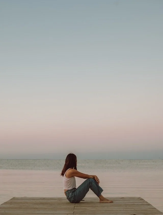 Woman sitting on a pier looking out at the sea