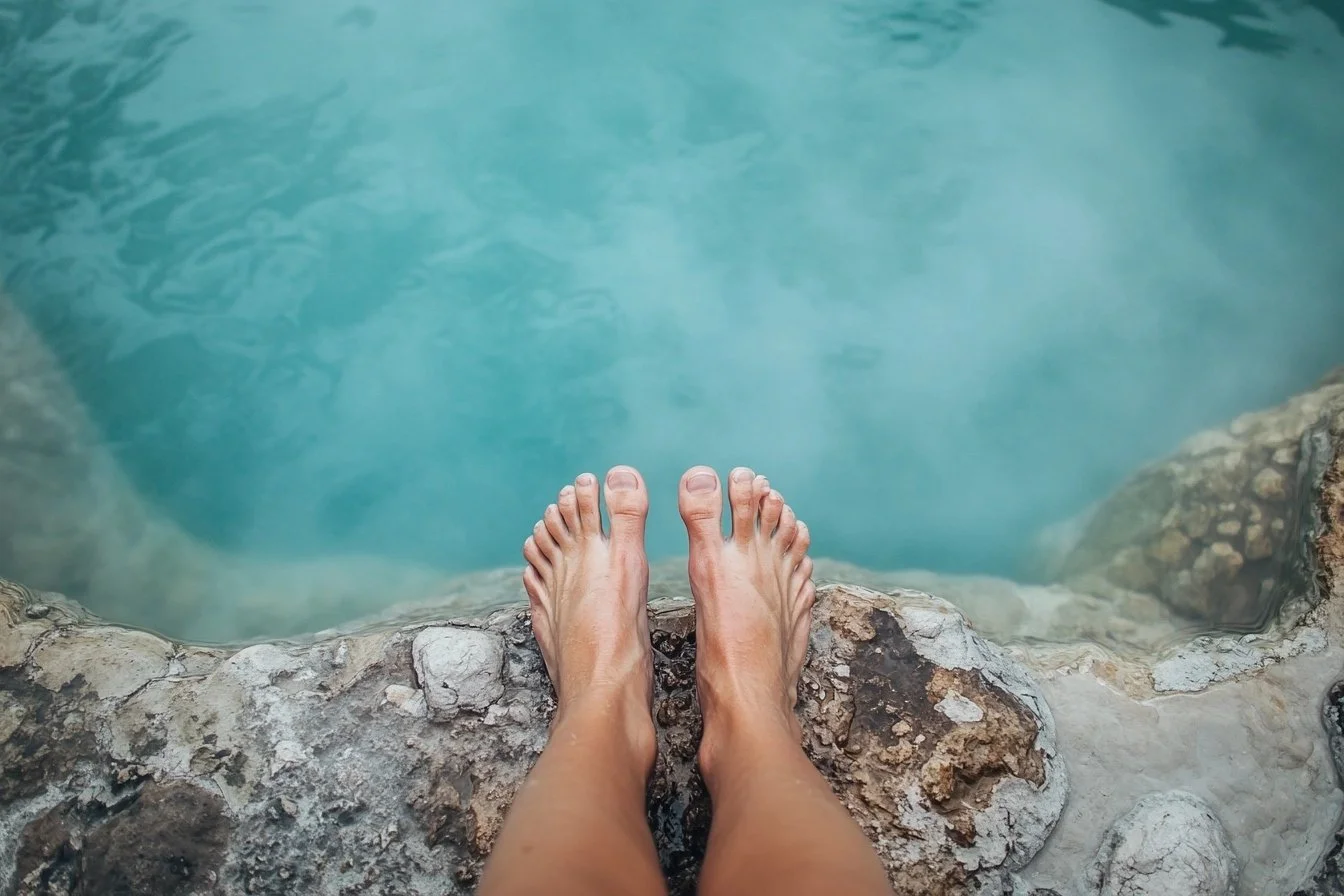 image of someone's feet standing on the edge of a thermal pool about to step in