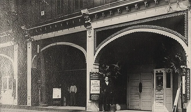 Sepia toned image of the Cascade Theatre from the early 1900s with two men in front