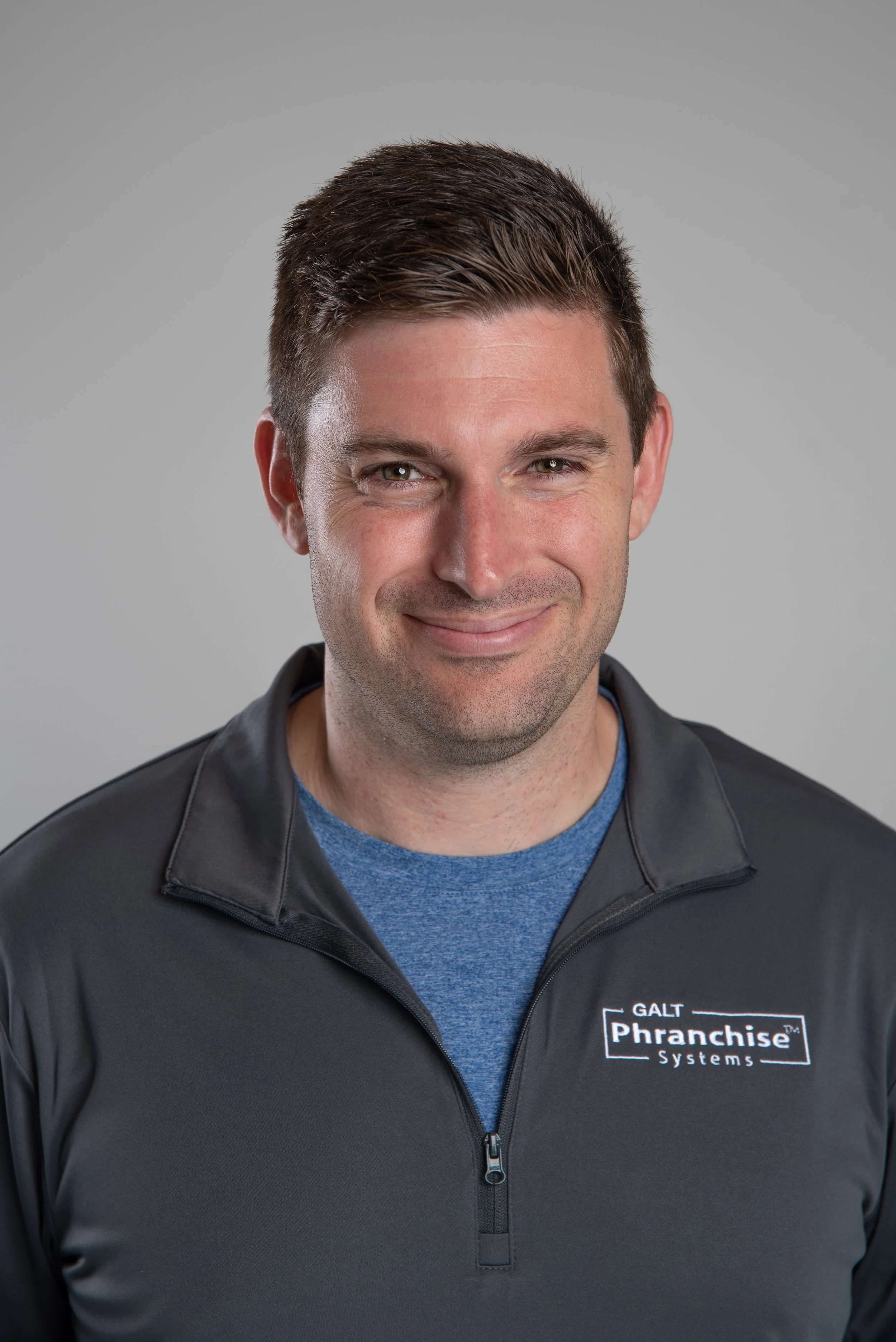Portrait of a man with short dark hair, wearing a black jacket with a "GALT Franchise Systems" logo, smiling against a plain background.