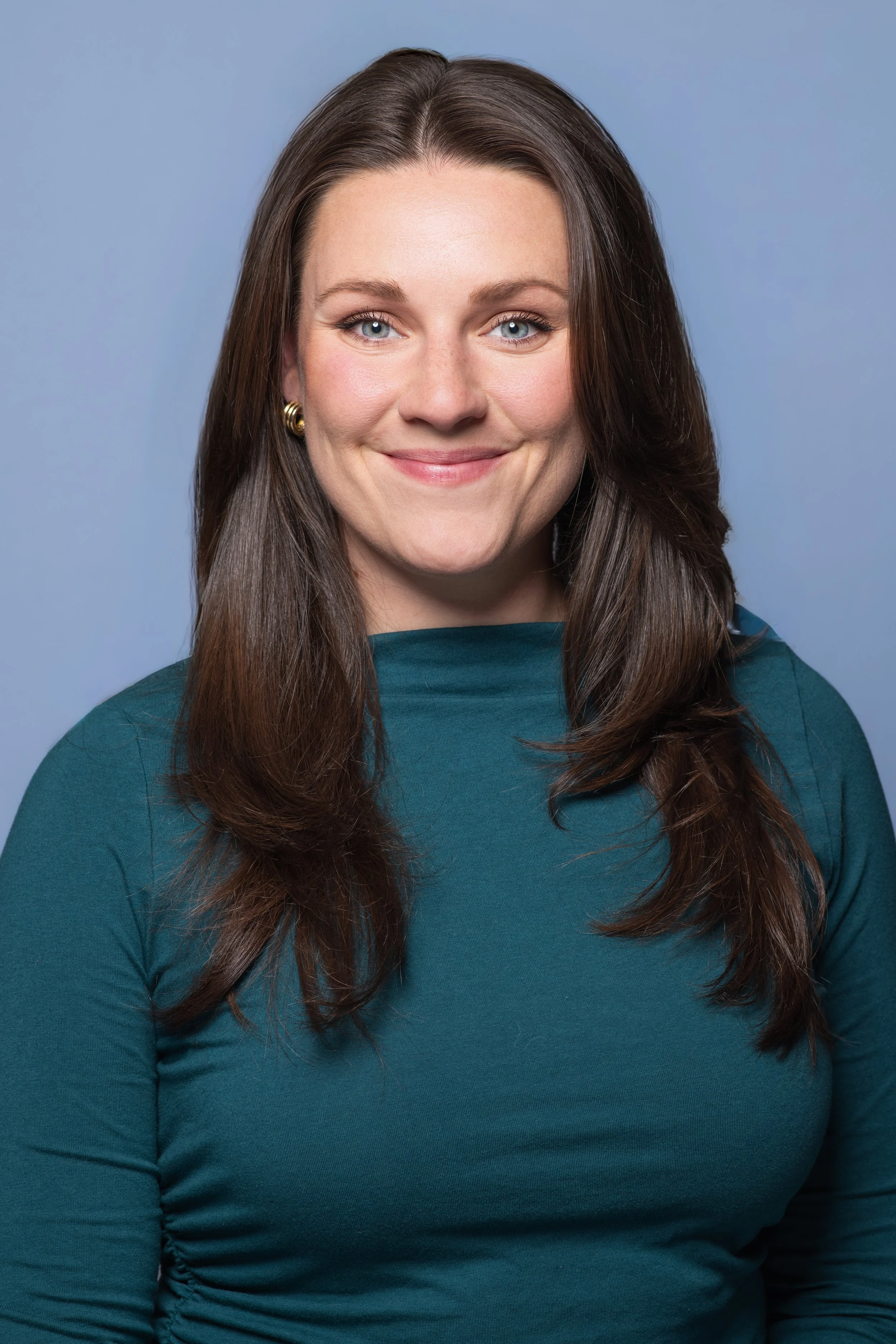 Professional headshot of a woman with a blue backdrop facing the camera head on wearing a green top.