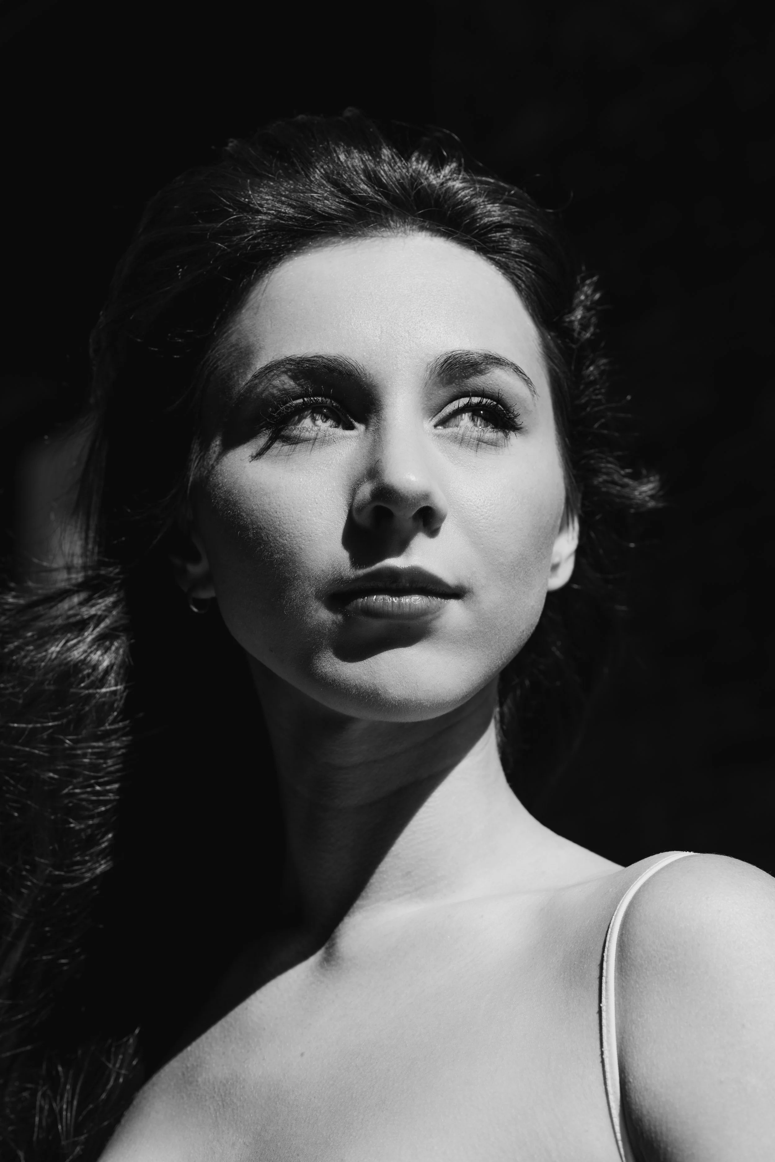 Black and white portrait of a woman with long hair, looking up and to the side, with light falling on her face.