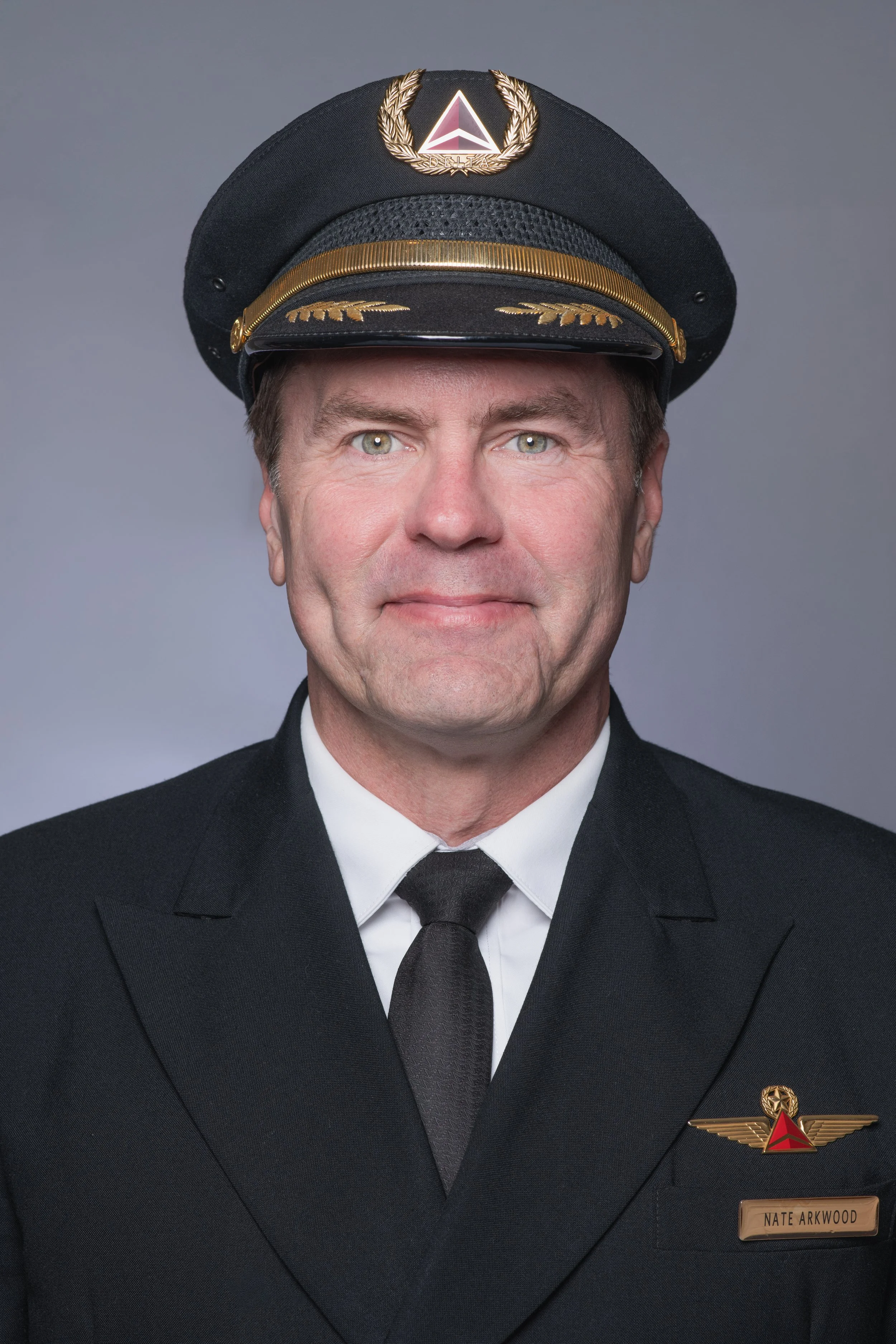 Professional headshot of a woman with a grey backdrop wearing a Delta airline pilot's uniform and facing the camera directly.