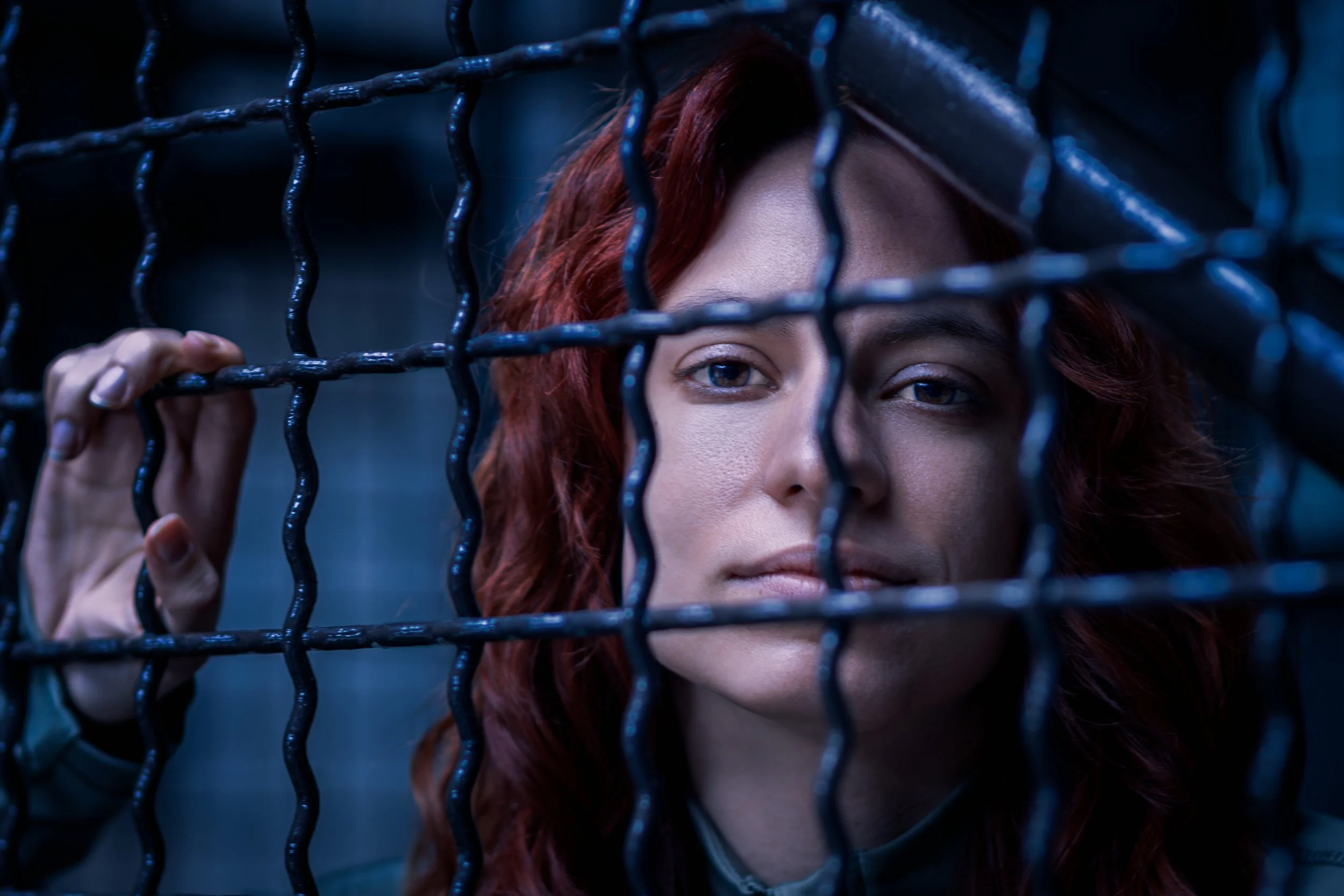 A woman with red hair looking through a metal fence.