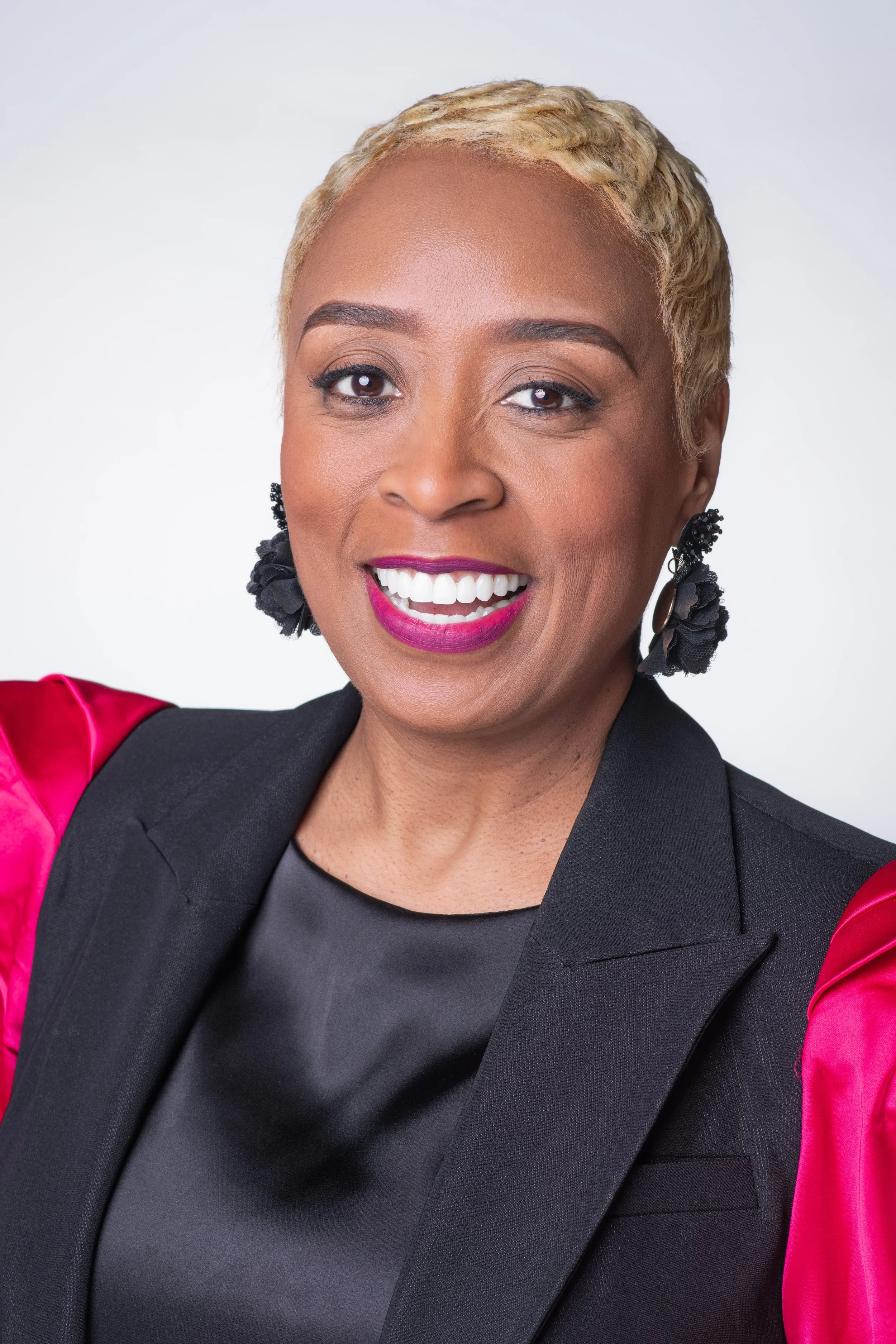 Professional headshot of a woman with a white backdrop wearing a black top with red sleeves. She is facing the camera.