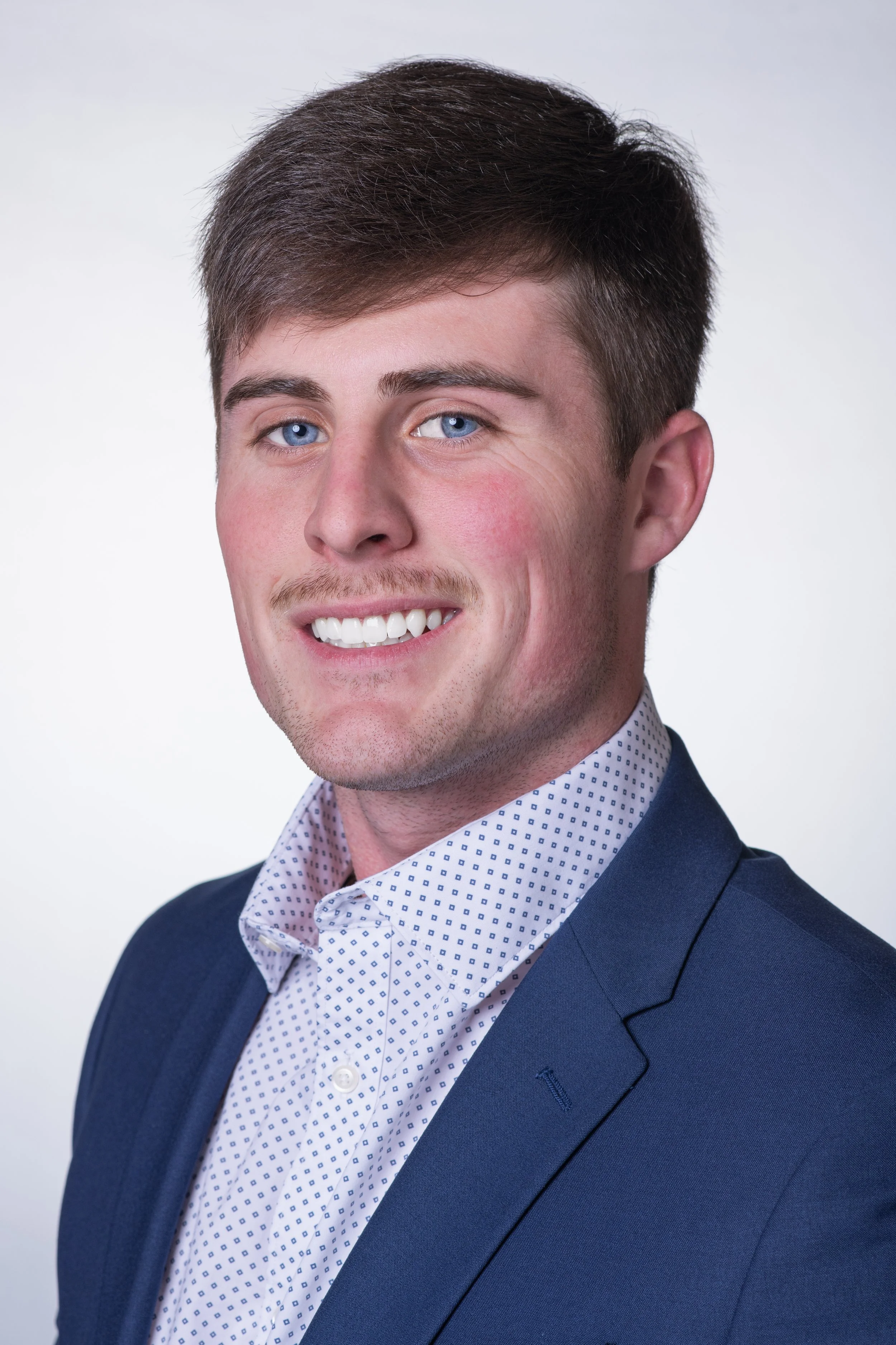 Professional headshot of a man with a white backdrop wearing a blue suit and facing camera left.