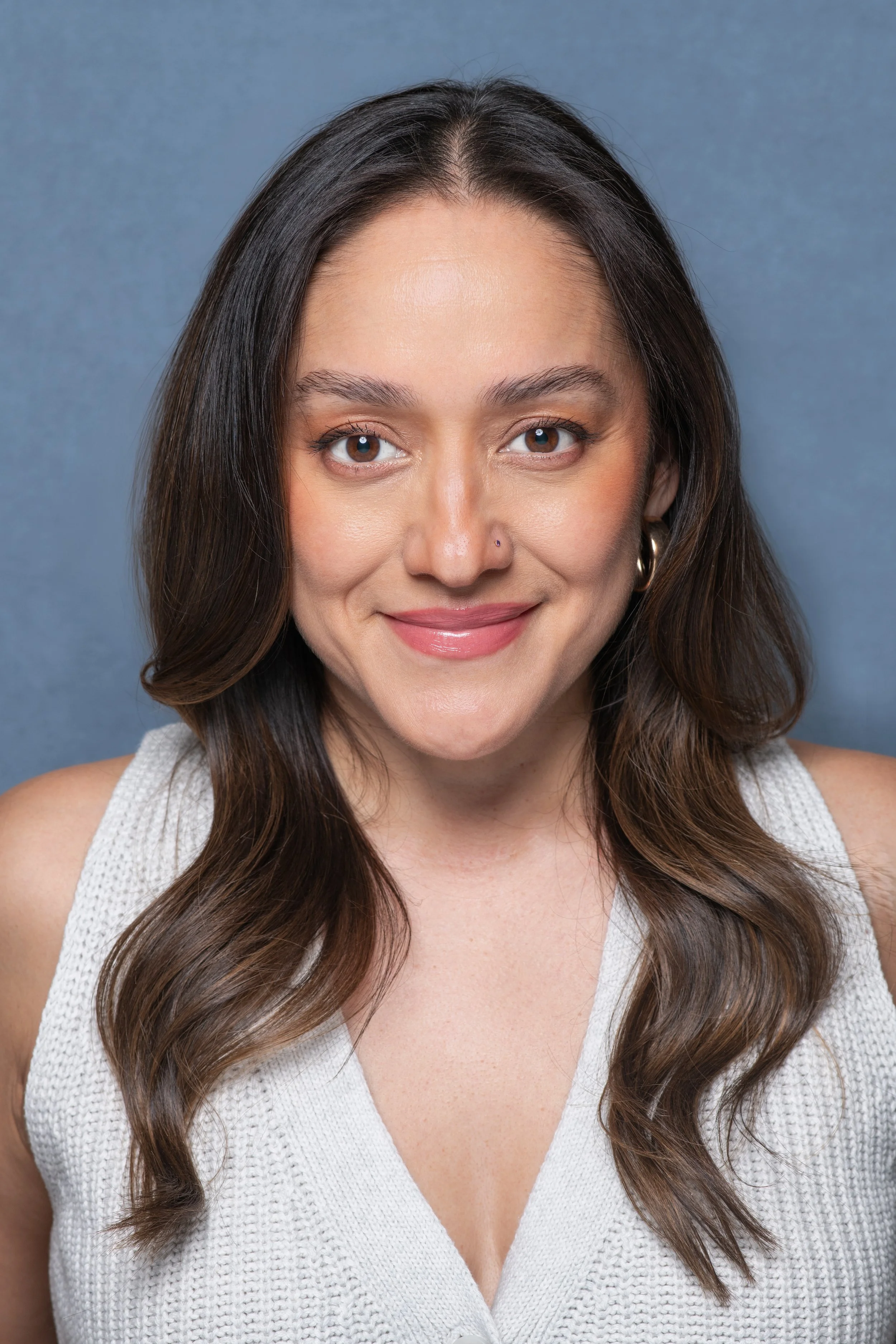 Professional headshot of a woman with a blue backdrop facing the camera directly and wearing a white sleeveless top.