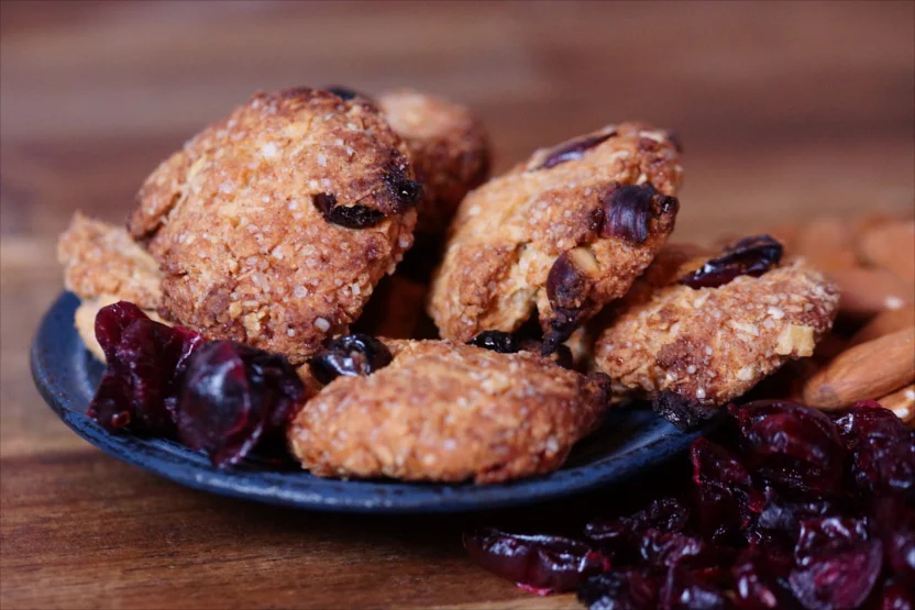 Ein Teller mit frisch gebackenen Müsli Cookies, dekoriert mit Cranberries und Nüssen, ideal als gesunder Snack für zwischendurch.