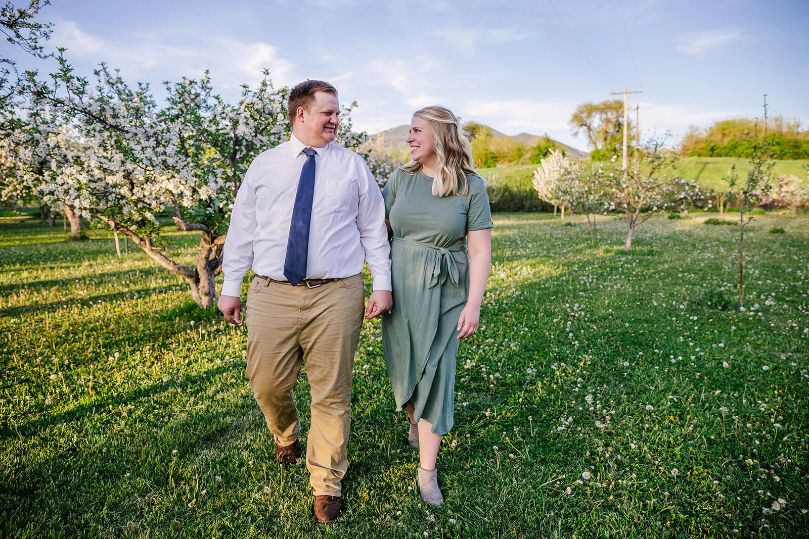 Mom and dad walk through field of flowers. Summer time photos. Looking into each other’s eyes. Family photos. Ranch style photography. Apple Orchard photography. Professional family photos. Twin parents. Trees blossoming. Tree blossoming photos. #twinparents #appleorchardphotography #summertimephotos #familyphtos #blossomphotos #lookingintoeachotherseyes #happyfamily #formalpictures #greenfieldphotos #hotsummernights
