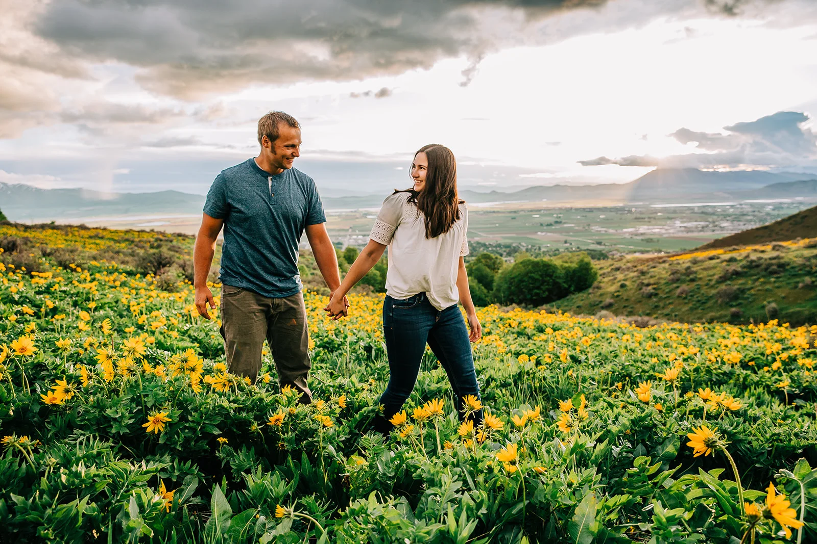 Beautiful sunflower field for photos. Mountain flowers. Mom and dad pose holding hands. Walking through a field of sunflowers. Happy families together. Holding hands walking through a field of flowers. Springtime mountain photos. Professional Family photos. #sunflowerfields #husbandandwife #mountainphotography #happyfamily #wildflowers #sunflowers #springtimephotos #momanddadphoto #familiestogetherforever