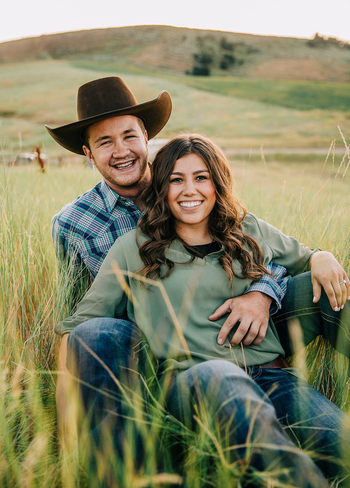  engagements sitting in a grass field happiest couple big smiles simple background small town love sitting poses couple poses bride to be casual outfit inspo summer engagement session engagement hairstyle inspo couple goals engagement outfit inspo ca