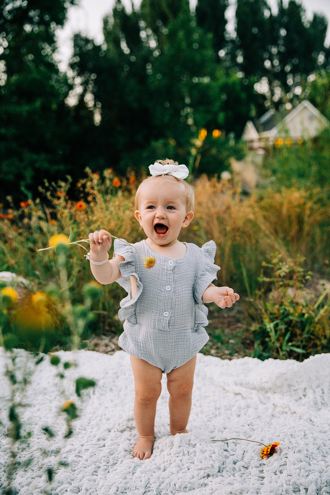  first birthday for baby girl kids fashion inspo what to wear to birthday photoshoot girl playing with wild flowers green back ground happy baby smiling baby blue eyed baby kids posing ideas how to get baby to smile Denzil Stewart park baby photograp