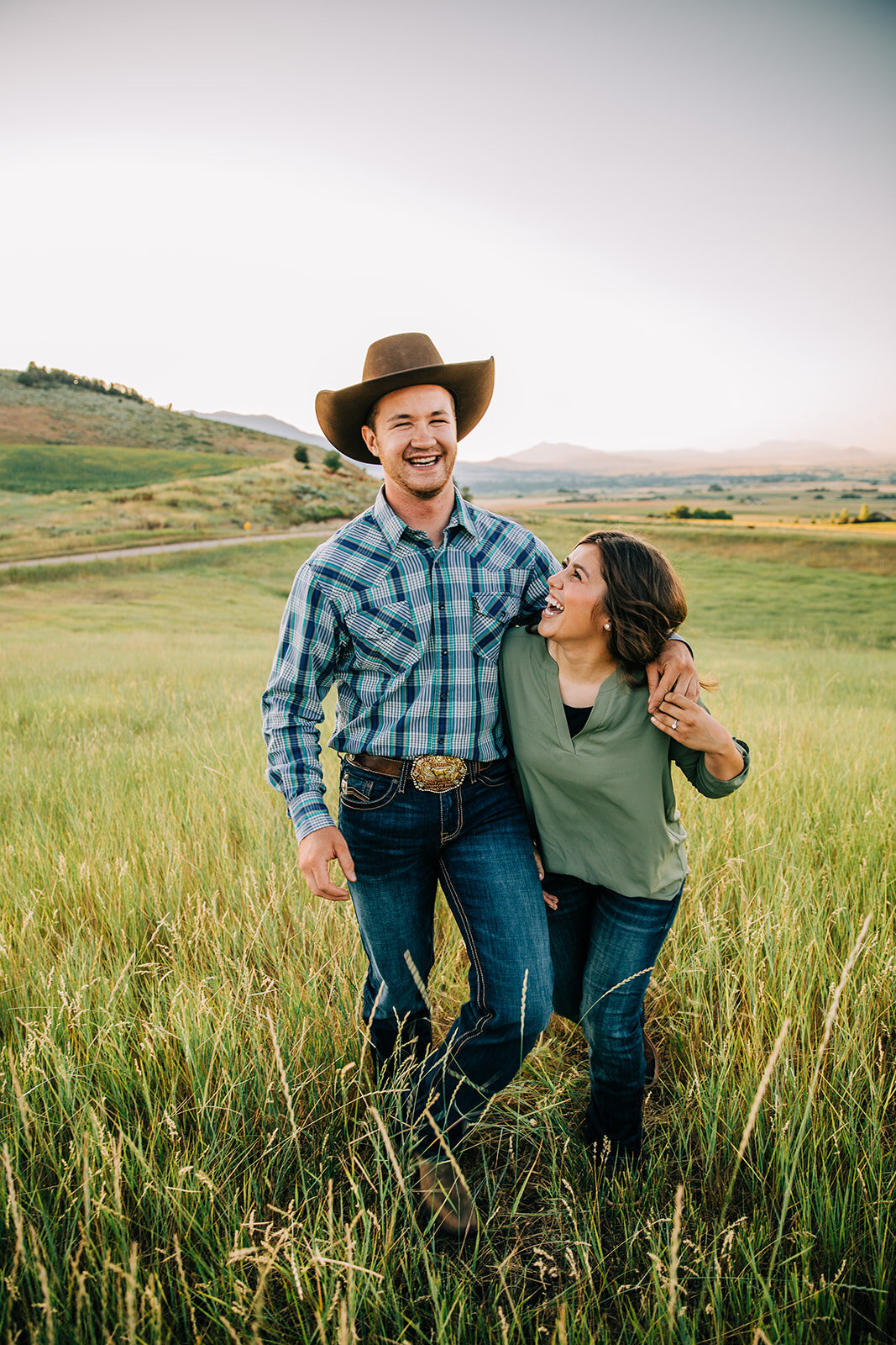  summer time engagement session walking posing ideas for couples casual outfit inspo what to wear to engagement session bright smiles laughing happy couple women hairstyle inspo hat styling ideas simple background green field and wildflowers paradise