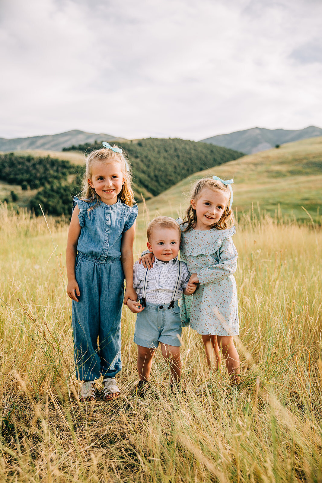  family pictures in hyrum utah toddlers young children siblings posing together cousins blue denim romper mint dress baby boy suspenders yellow fields rolling green hills summer family photos grandchildren bella alder photography utah family photogra