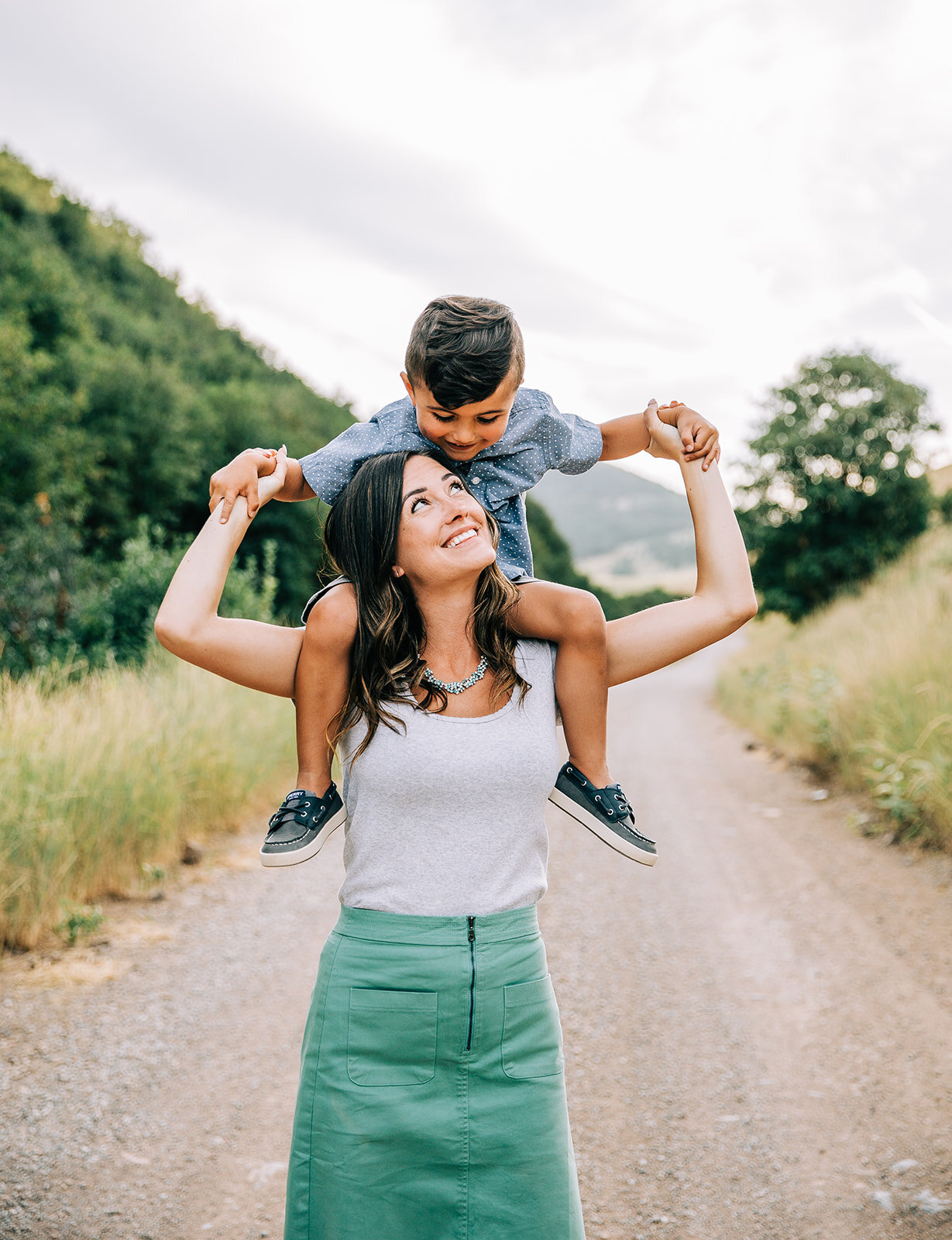  mom and child posing piggy back ride young boy on his mom’s shoulders teal skirt blue button up toddler outfit coordination for family pictures shades of blue and green matching color scheme outfit inspo for family photography with professional fami