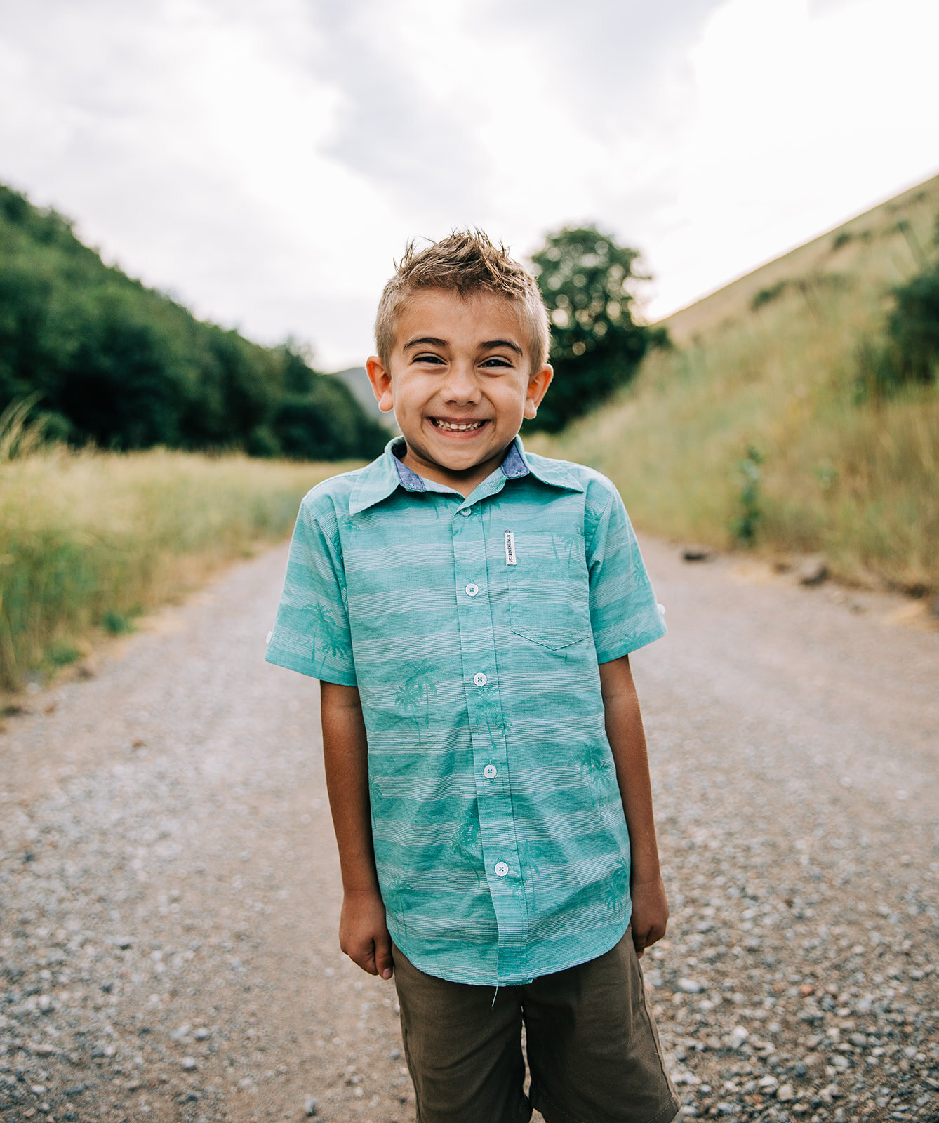  cheeser grin young boy posing for individual portrait during extended family pictures with large family cousins child portraits cache valley family photographer teal striped button-up shirt outfit ideas for big group family pictures in cache valley 
