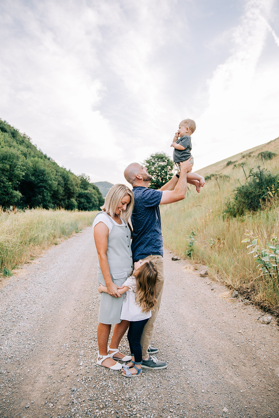  young family small family of four individual portraits during extended family picture session in paradise utah hyrum utah family pictures young girl baby boy dad holding son up in the air mom holding hands with daughter pose ideas for family picture
