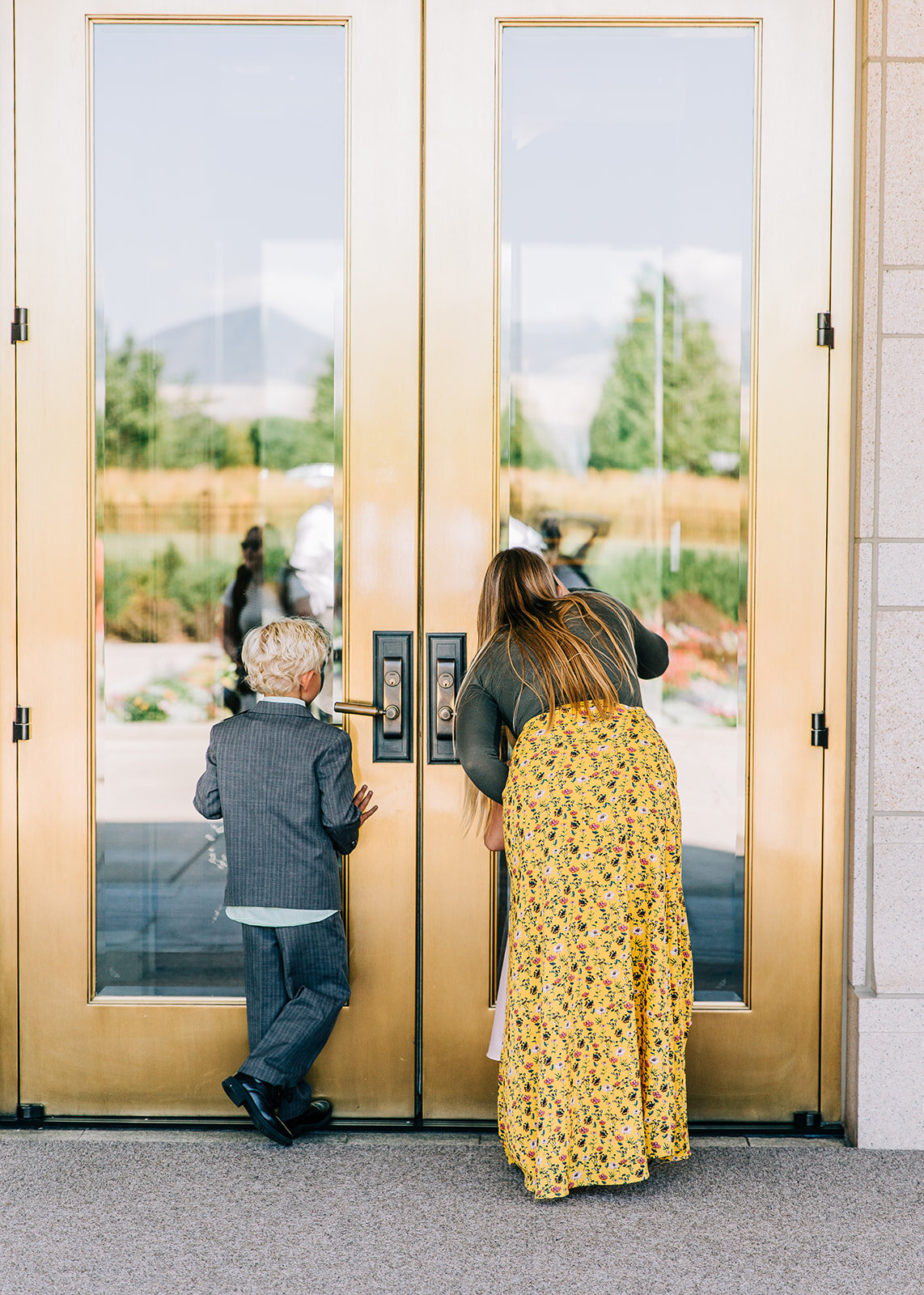  young boy and girl peeking in the windows of the temple waiting for the bride and groom to exit lds family lds wedding sealing ceremony mormon wedding gold doors salt lake city temple marriage lds wedding photographer oquirrh mountain temple south j