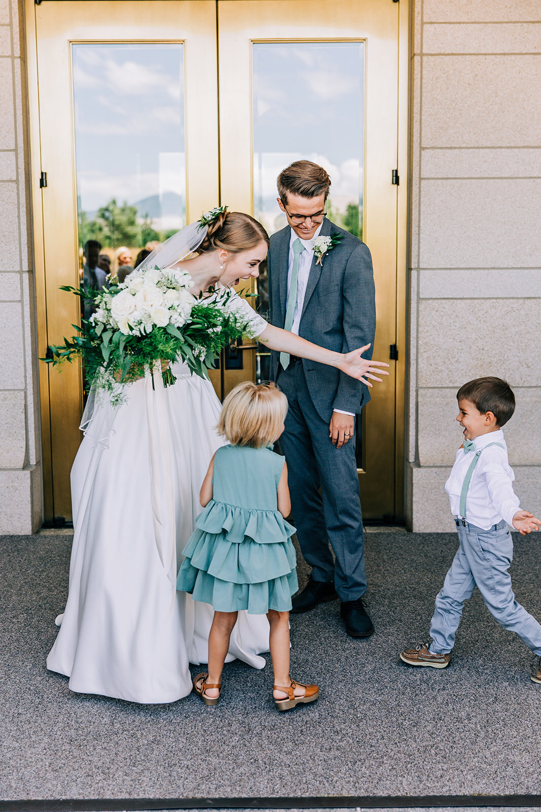  bride hugging young children welcoming in nieces and nephews after the sealing oquirrh mountain temple south jordan utah wedding white and green floral inspo summer wedding charcoal tux grey and mint light blue wedding colors gold door salt lake cit