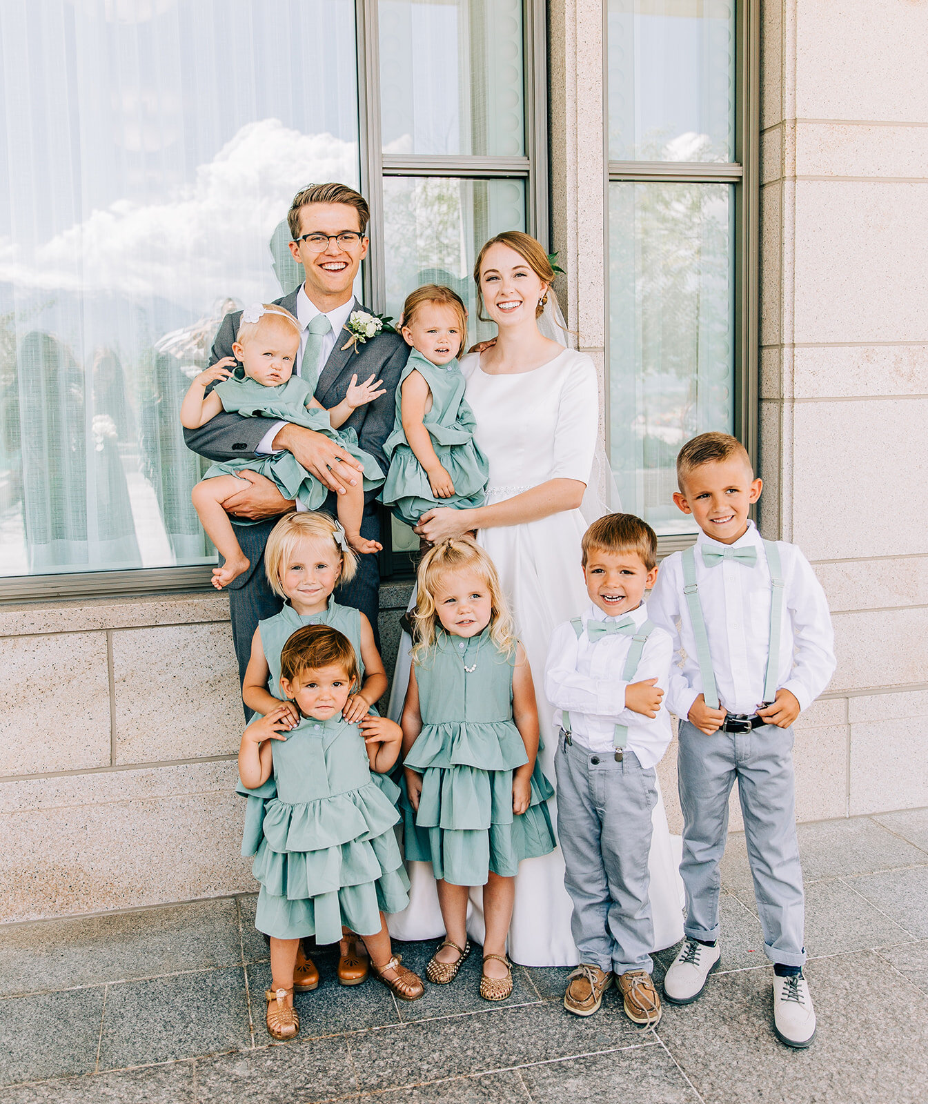  bride and groom posing with nieces and nephews part of the wedding party young kids with the bride and groom ruffle dresses light blue mint wedding color scheme sea green wedding inspo summer wedding ideas bowties and suspenders for little boys affo