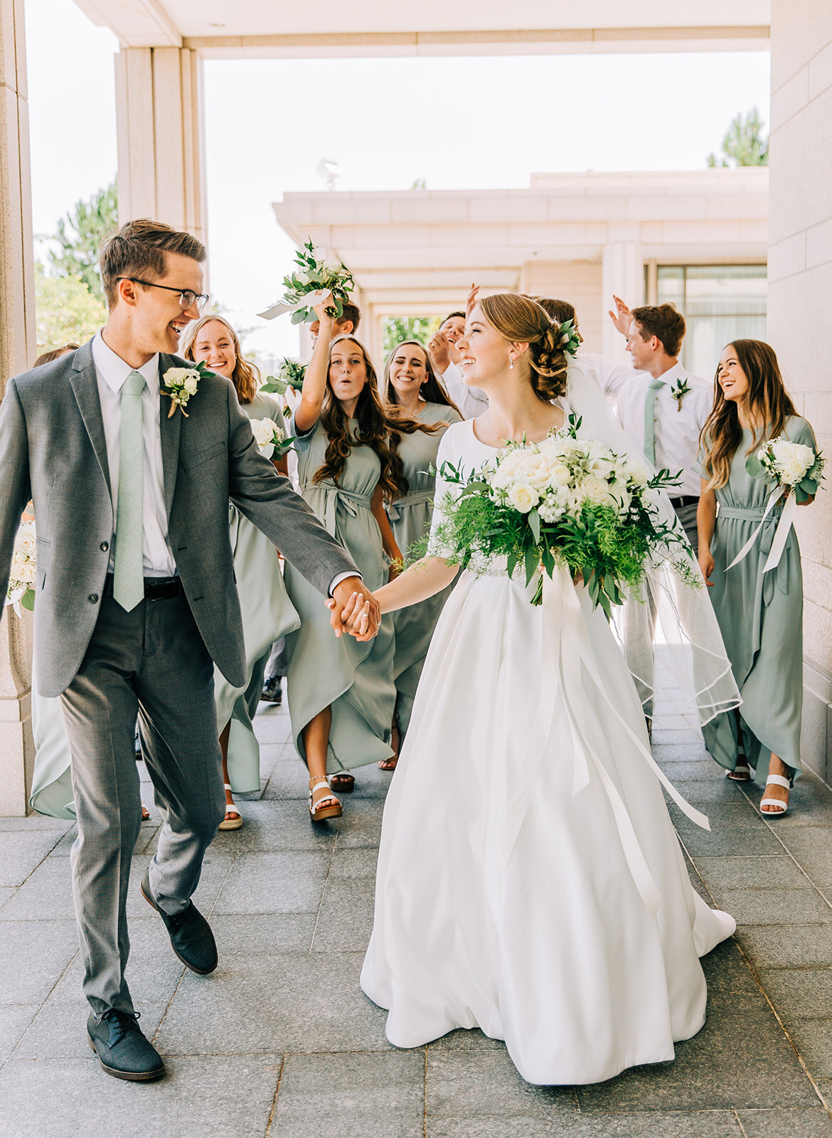  bride and groom holding hands walking away from their wedding party friends as they look into each others eyes and their friends cheer behind them green and white floral bouquet wedding bouquet inspiration for wedding florals mormon wedding seagreen