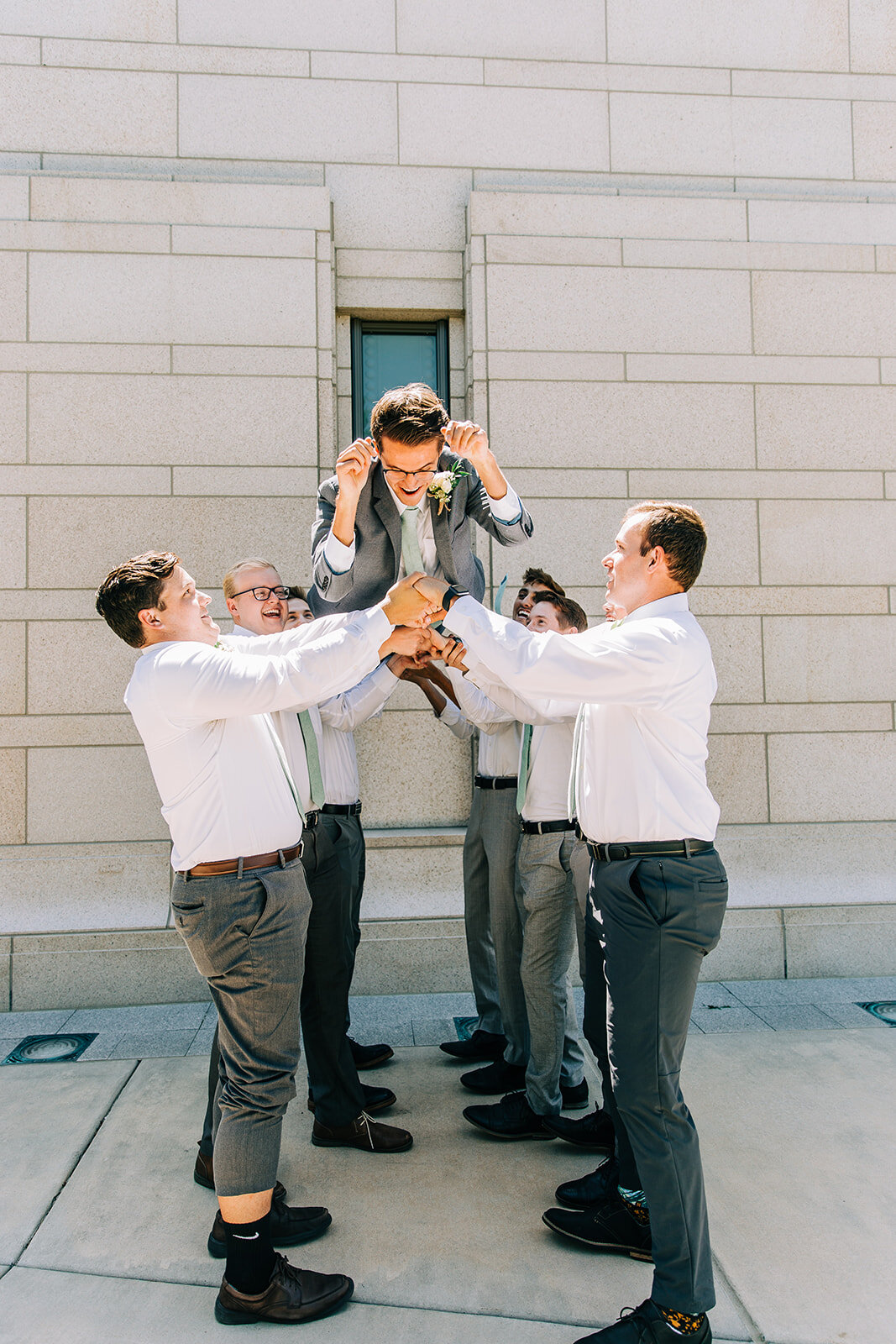  groomsmen tossing the groom up in the air wedding party grey suit oquirrh mountain lds temple wedding professional wedding photography sunny summer day summer wedding inspo wedding party pose ideas pictures with friends and family outside the temple