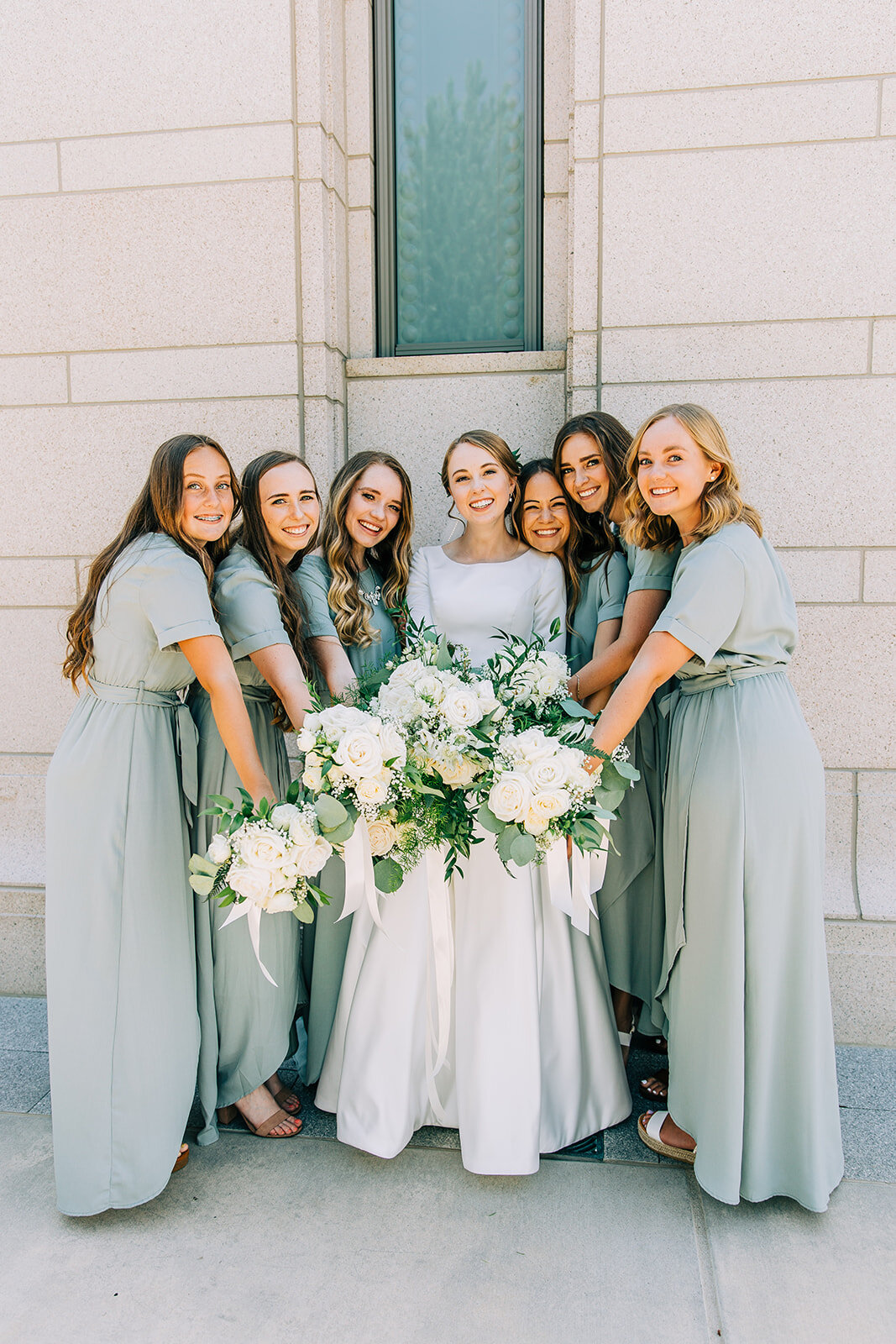  bride posing with her bridesmaids holding bouquets out in a circle white and green florals wedding bouquet inspiration for summer wedding white and grey and sea green wedding color scheme professional wedding photography on a budget from affordable 