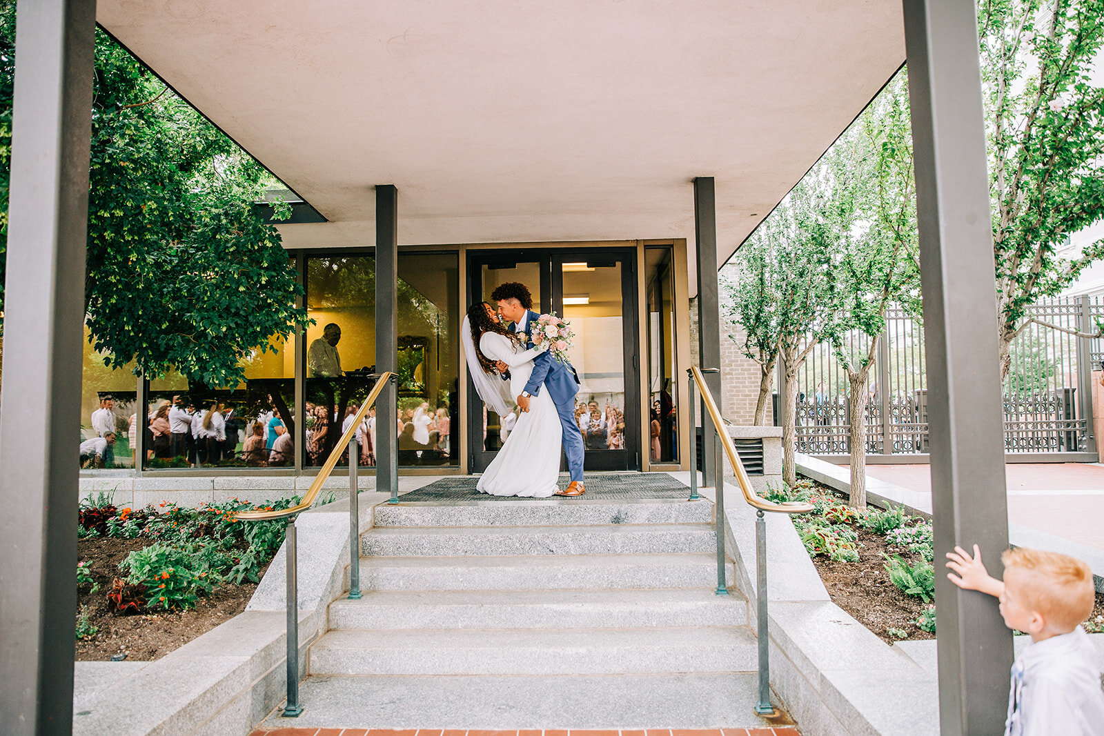  bride and groom kissing on the temple steps during their temple exit from the lds salt lake city utah temple in temple square professional wedding photographer affordable wedding photos long veil blue suit groom style curly hair wedding hair ideas #