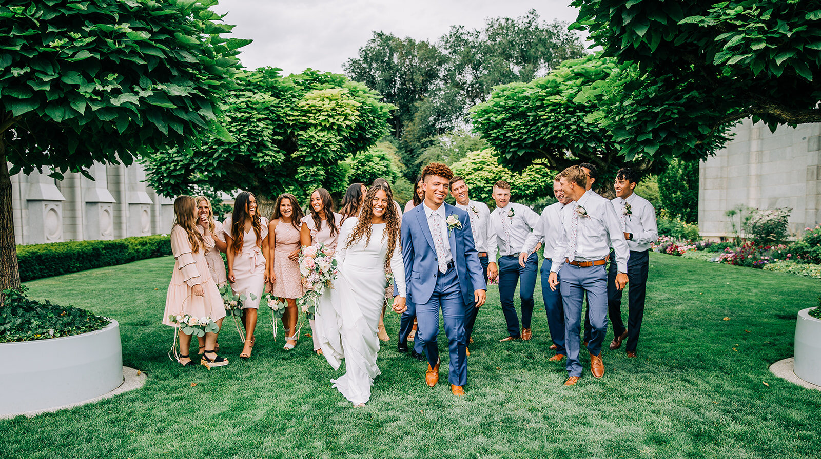  bride and groom blue suit wedding party pose ideas walking towards the camera groomsman white button up blue grey pants bridesmaid in blush pink dress friends and family new husband and wife wedding party photos professional photography for your wed