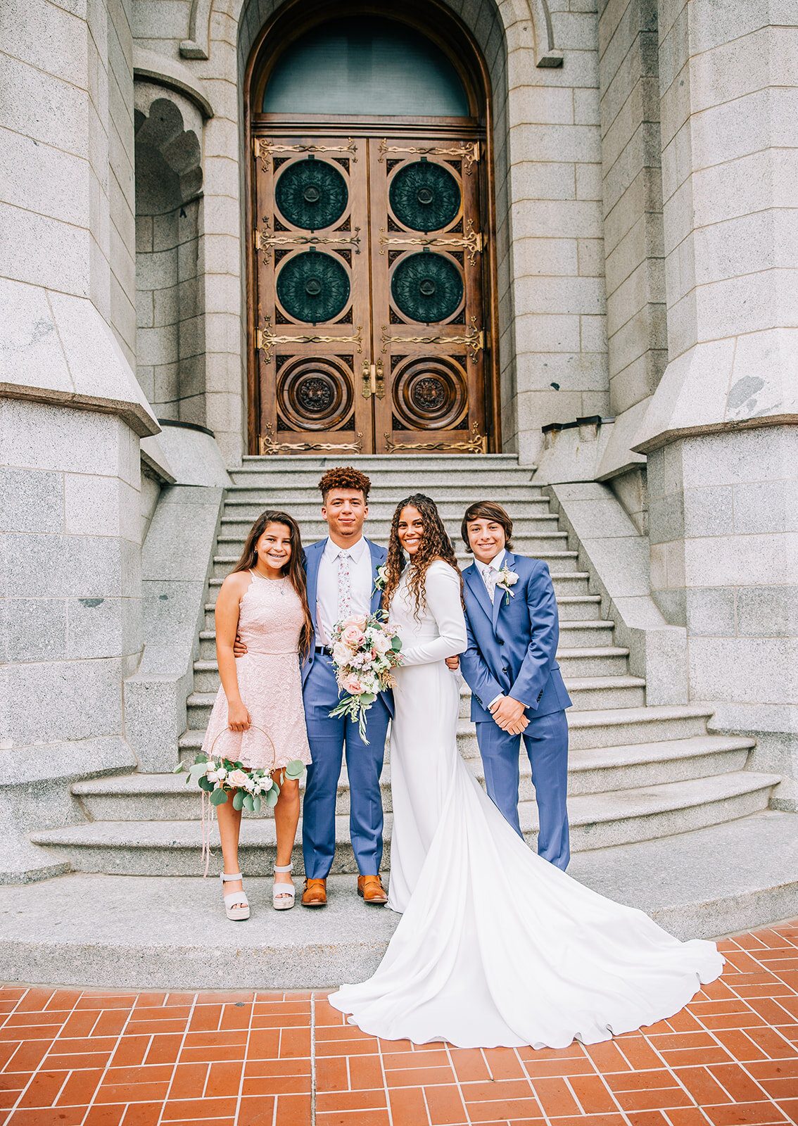  bride and groom standing with family blue suits wedding day style inspiration temple steps salt lake city utah wedding photographer blush dress long sleeve wedding gown bridal ensemble inspiration for curly hair brides young mormon newlyweds bride a