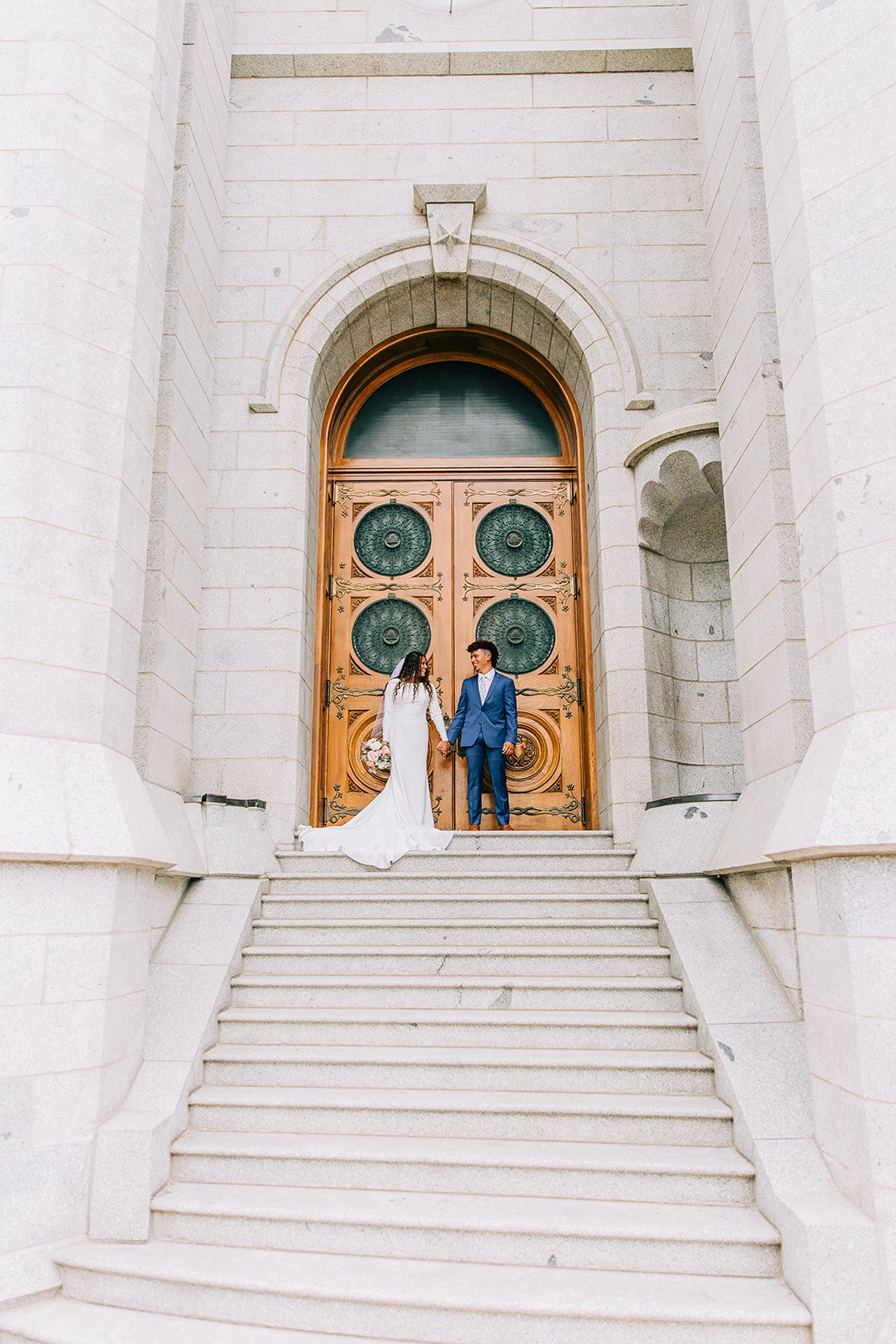  bridals bride and groom holding hands at the top of the stairs big beautiful door salt lake city utah lds temple pictures wedding day photos bridals stairs temple square professional wedding day photography bella alder affordable wedding photographe