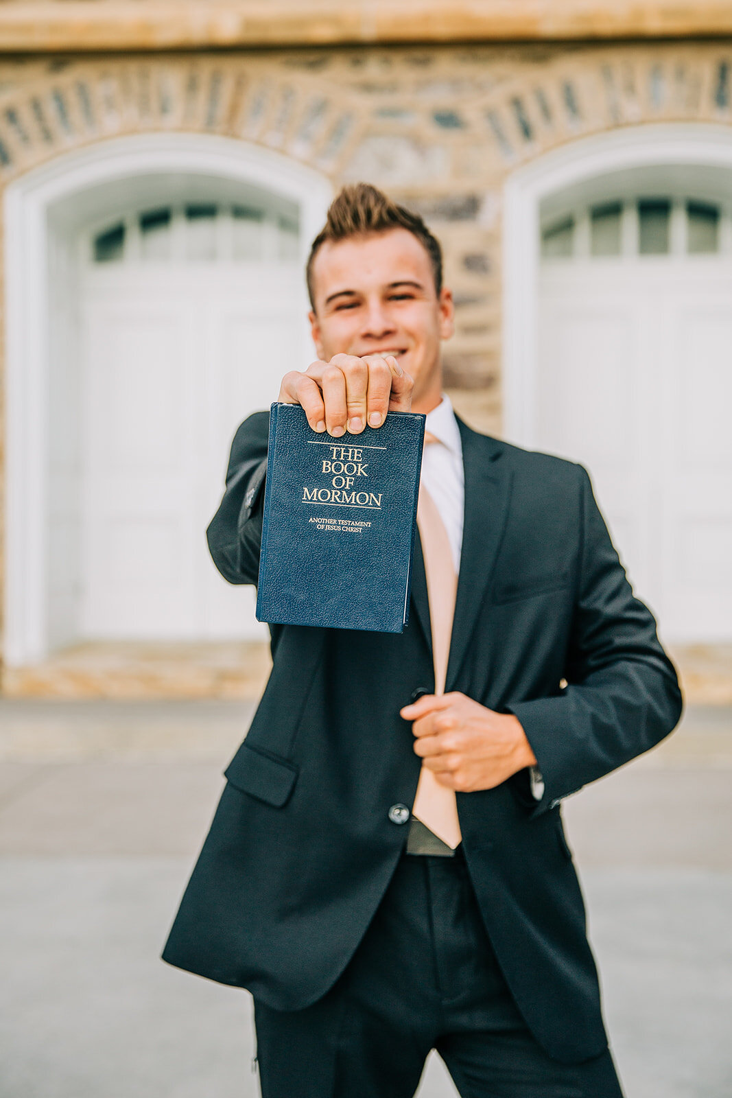  professional missionary photos of elder pritchett logan utah lds temple serve a mission missionary holding out a book of mormon for the camera black suit with peach tie missionary portrait session young man new elder I hope they call me on a mission