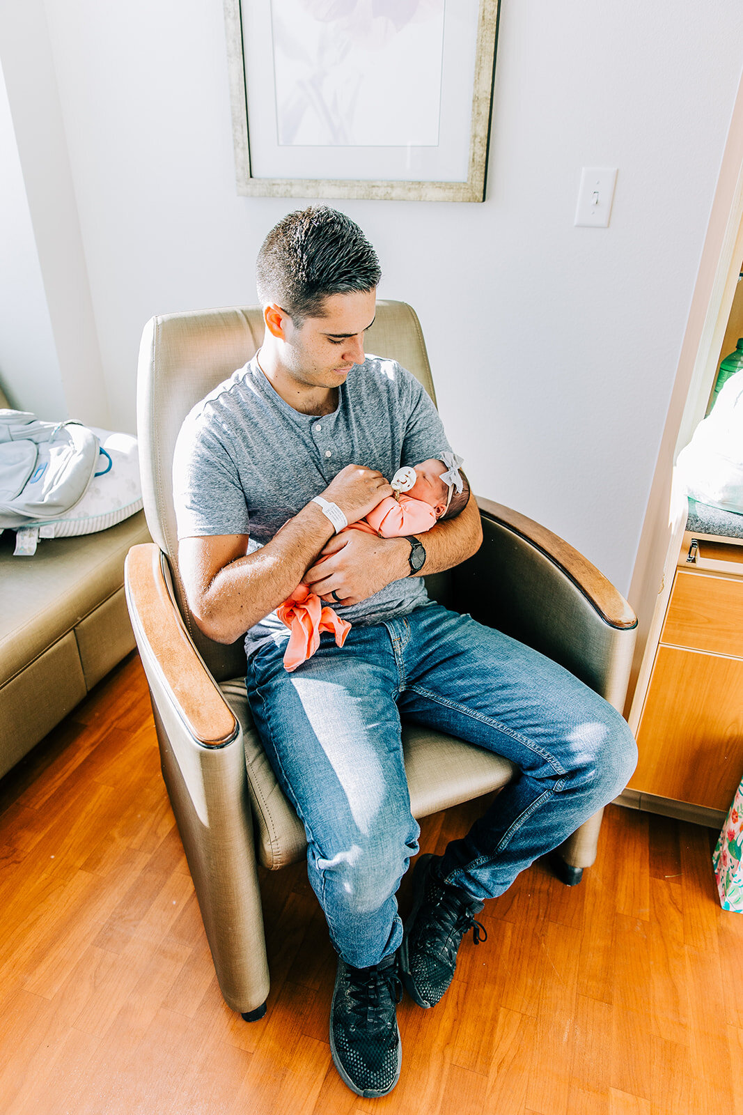  newborn photos shot with dad holding new baby girl in a pink swaddle in hospital chair logan regional hospital labor delivery room birth story professional newborn photographer bella alder photography fresh 48 photos in hospital room after baby’s bi