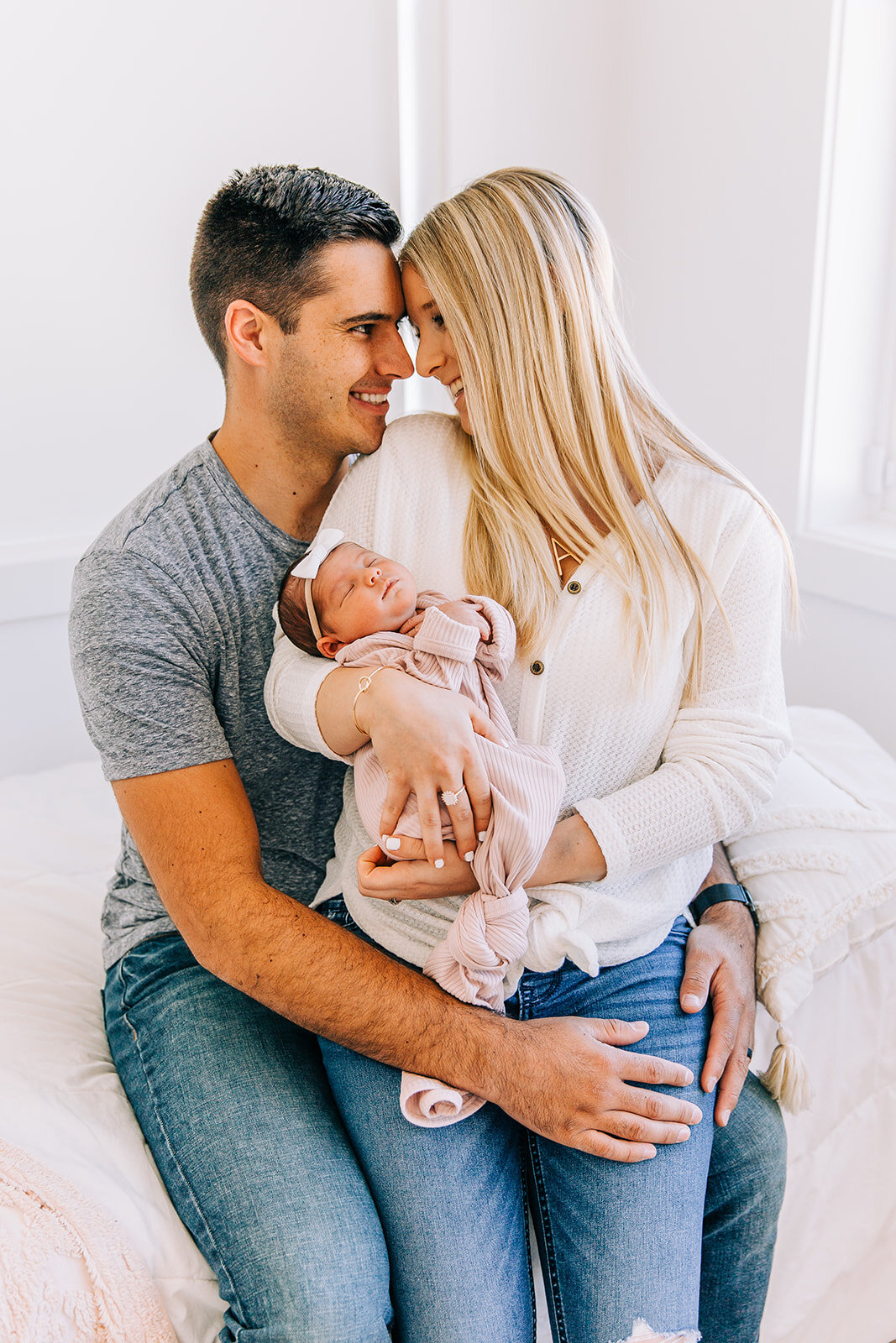  adorable picture of new family small family young parents first time parents mom and dad looking into each others eyes holding new baby girl newborn photography logan utah blush door studio pink baby dress natural light studio indoor photos newborn 