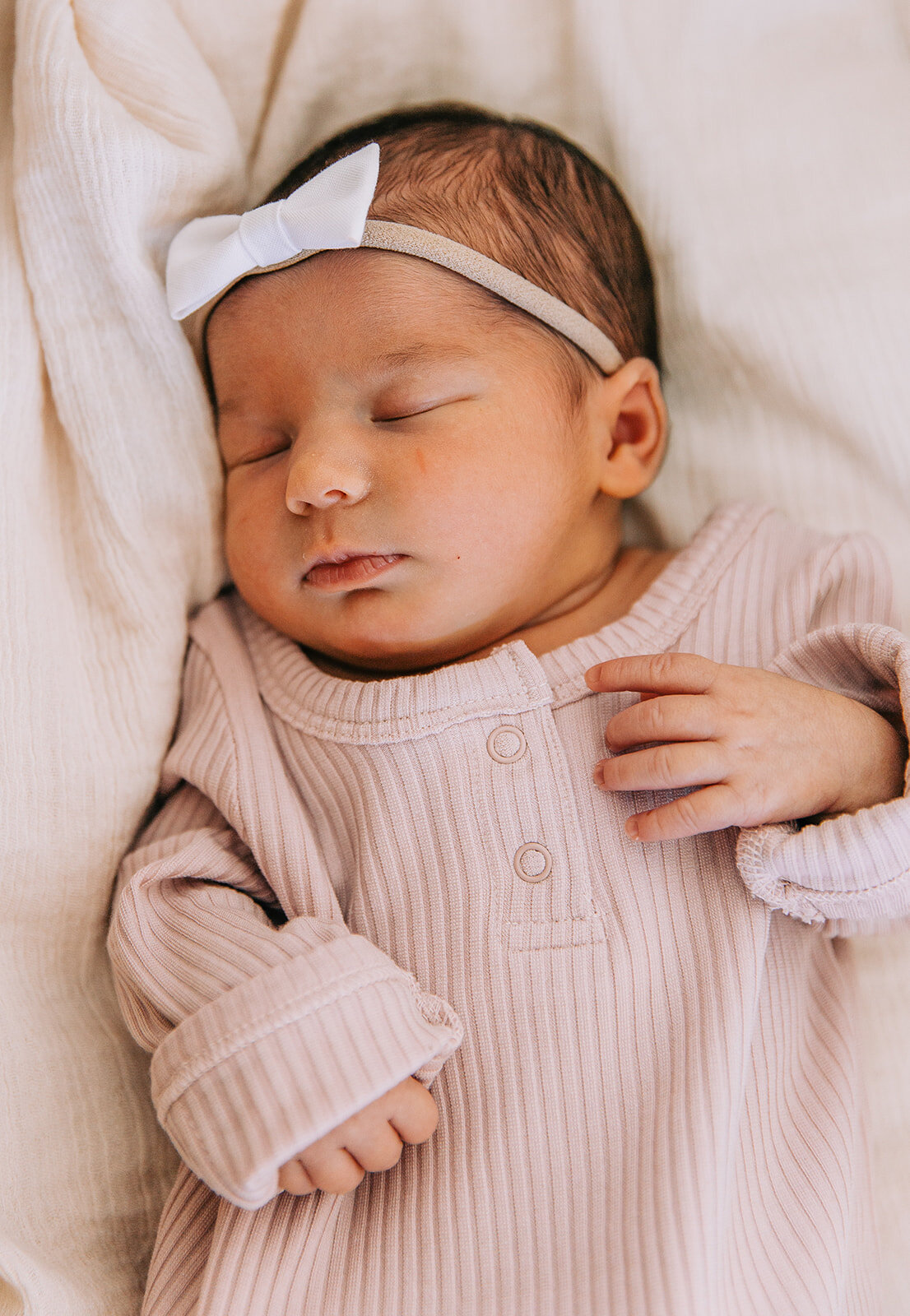  newborn baby girl in pink dress cream sheets white headband bow on her forehead sleeping baby during newborn session professional newborn photographer in logan utah blush door studio photography affordable studio session with bella alder photography
