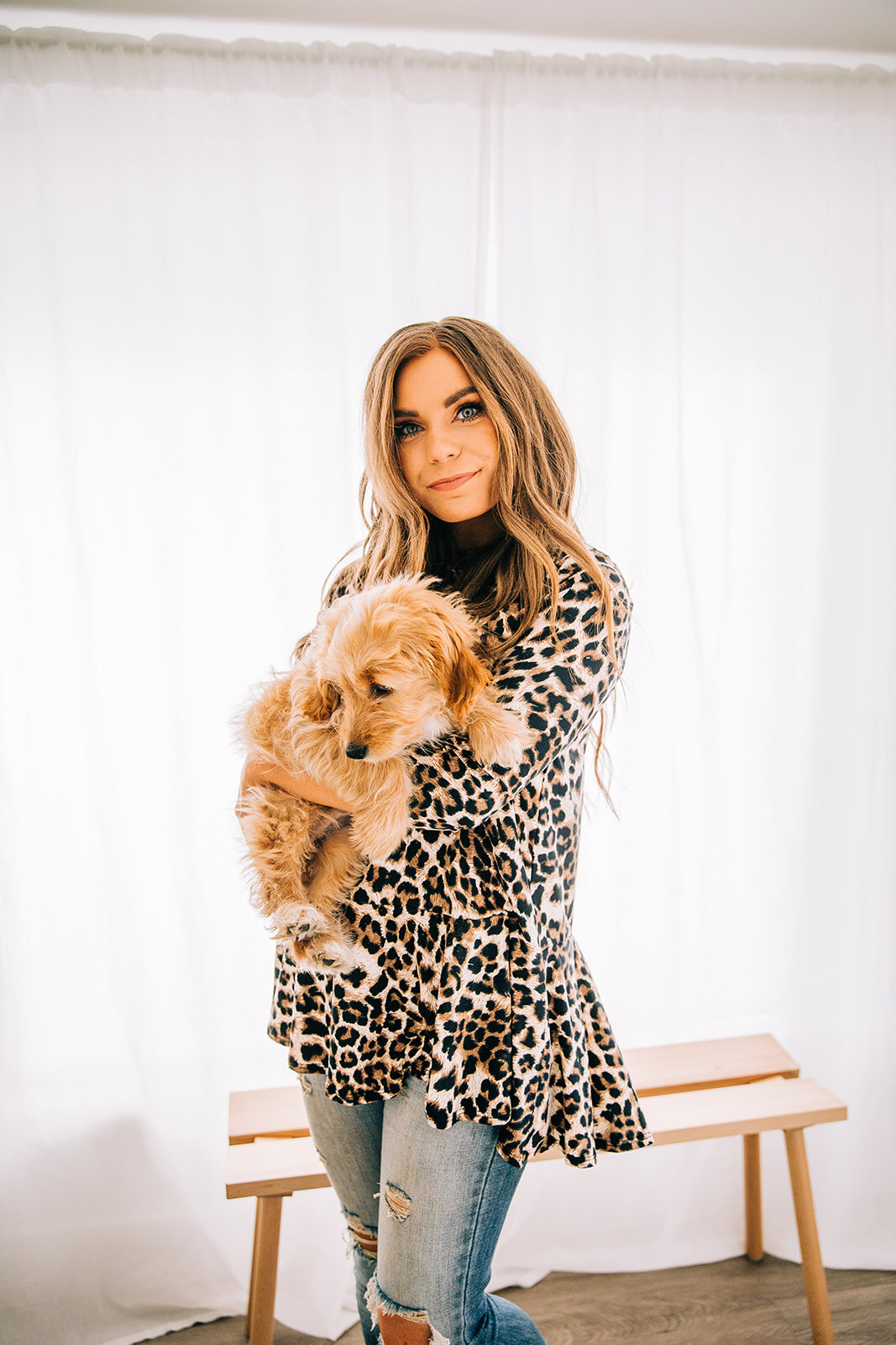  cheetah print leopard print patterned top holding a puppy at a photoshoot for online clothing boutique copper lane commercial photography distressed light wash jeans station studio backlist serious model face playing with dog at photoshoot for cloth
