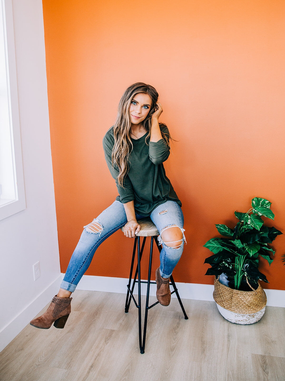  green fashion top long sleeves distressed jeans coral wall in natural light studio wedge booties model with beachy waves light brown hair sitting on a stool station studio logan utah bella alder photography product photos in logan utah #onlineshoppi