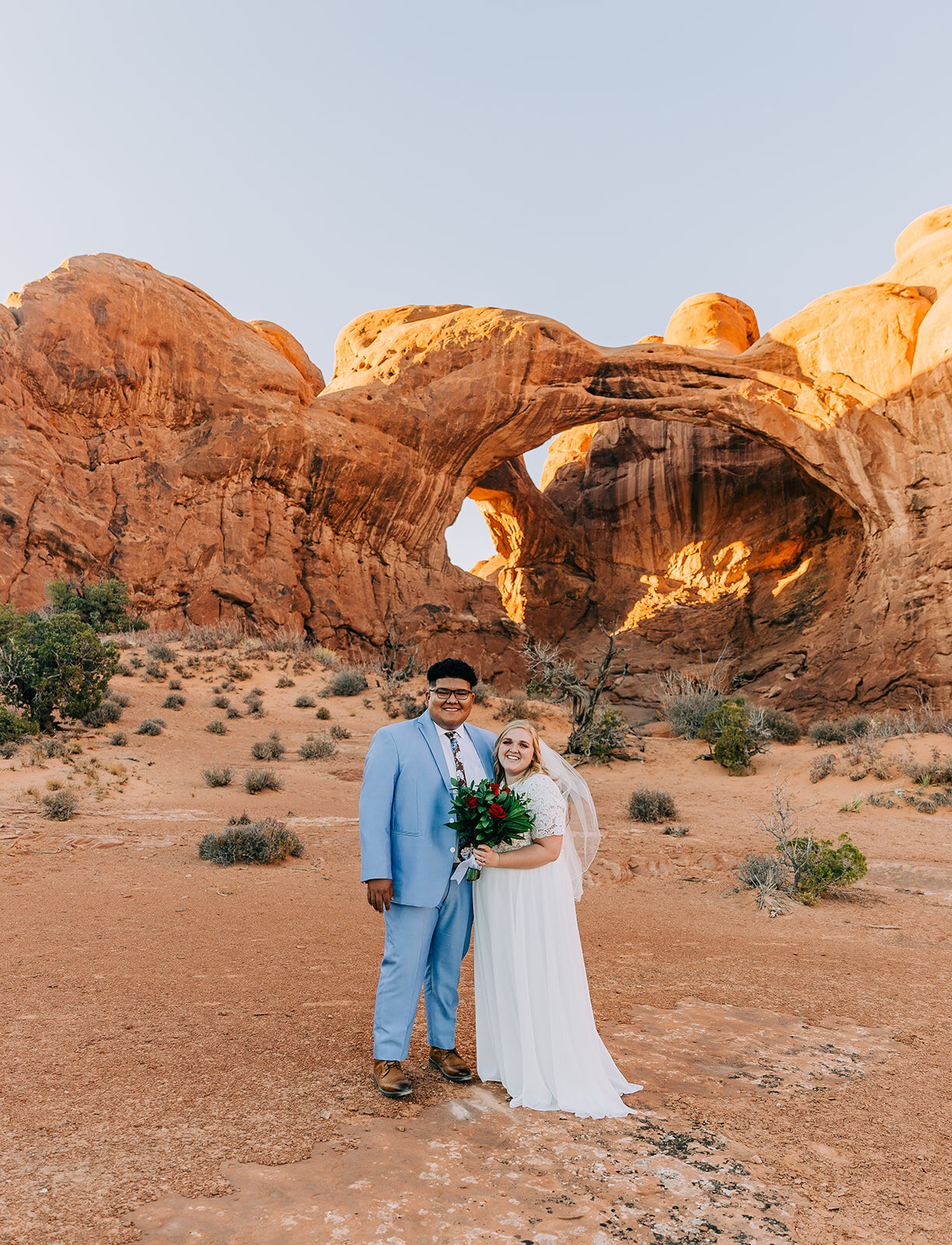  bride and groom hugging pose inspiration desert moab utah powder blue suit groom fashion bridal fashion modest wedding dress white dress veil bouquet inspiration double arch elephant rock professional photographers in utah utah wedding photographers