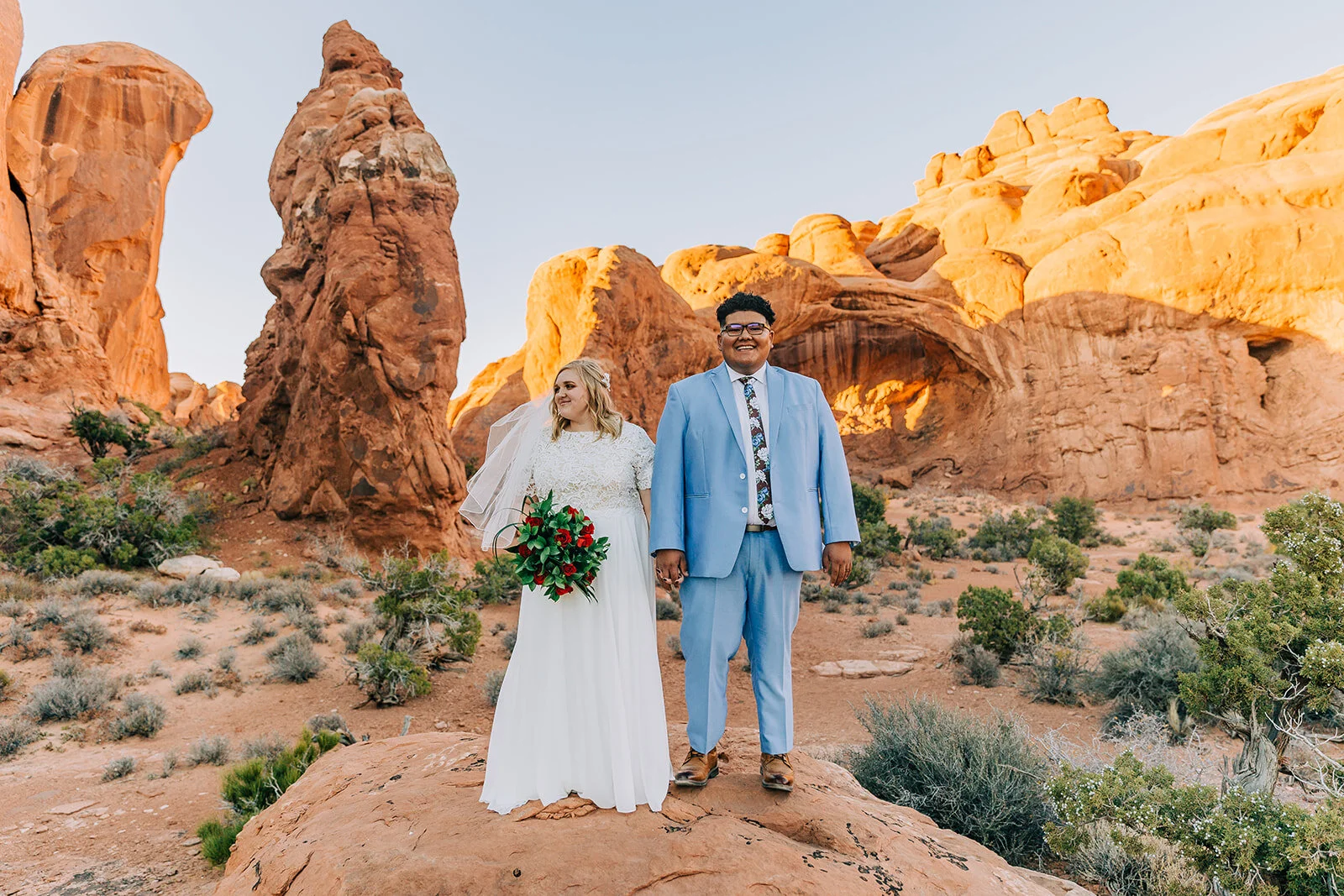 bride and groom hand holding pose inspiration desert moab utah groom smiling powder blue suit groom fashion bridal fashion modest wedding dress white dress veil bouquet inspiration double arch elephant rock professional photographers in utah utah we…