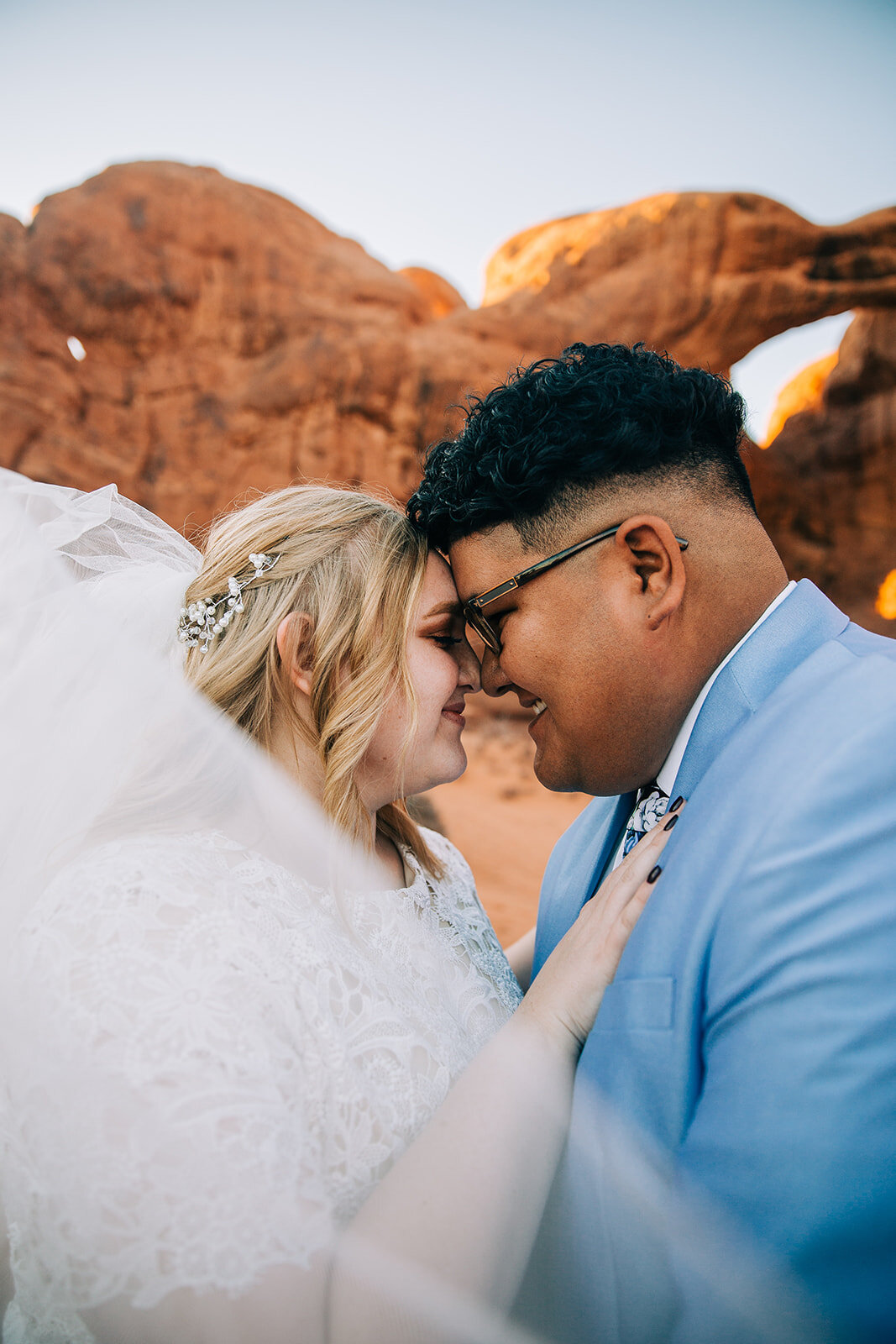  bride and groom snuggling veil shot kissing pose inspo desert moab utah groom smiling powder blue suit groom fashion bridal fashion modest wedding dress white dress veil bouquet inspiration double arch elephant rock professional photographers in uta