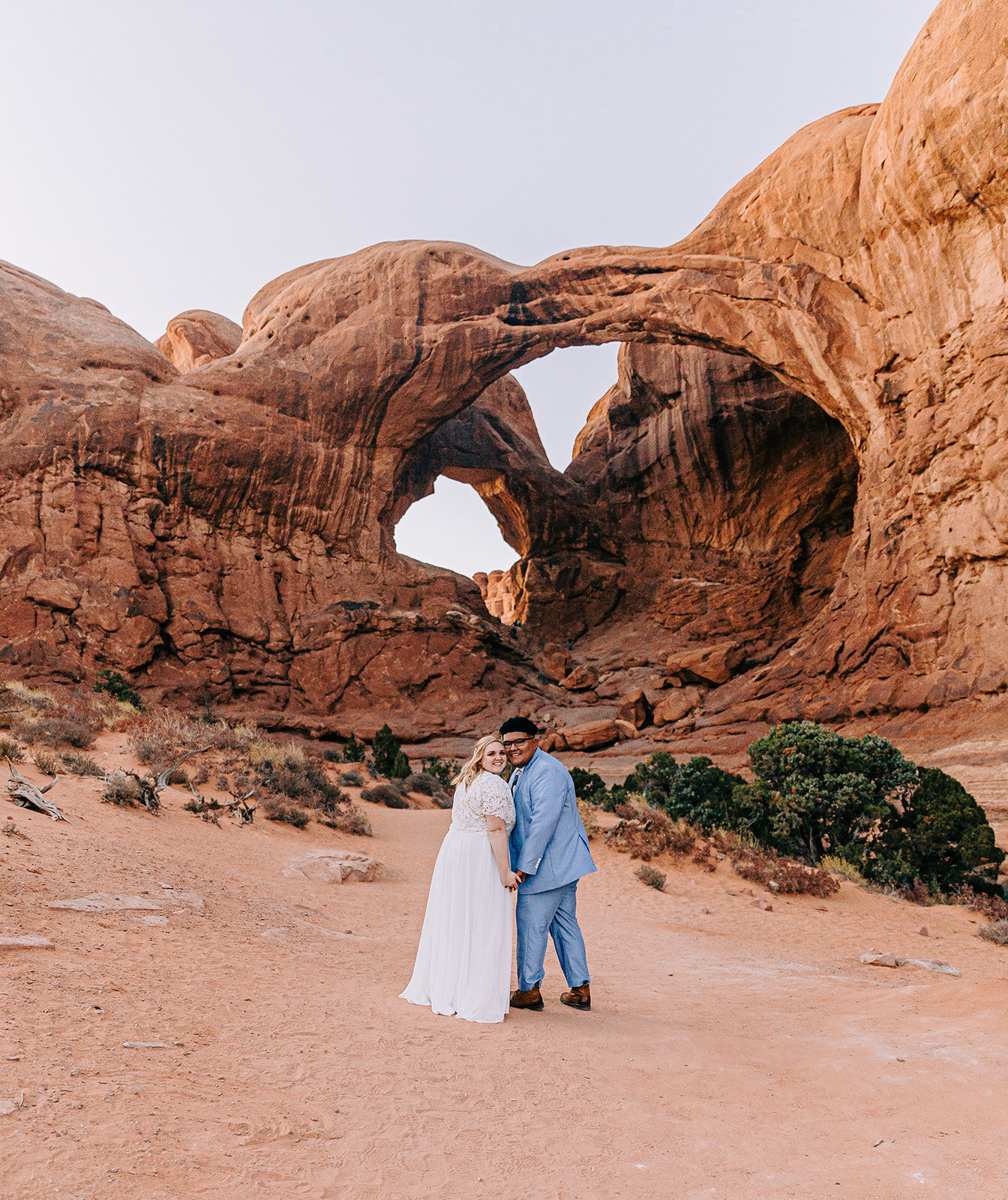  couple cuddling and smiling pose moab utah groom smiling powder blue suit groom fashion modest wedding dress wedding dress inspiration white dress veil bouquet inspo double arch elephant rock professional photographers in utah utah wedding photograp