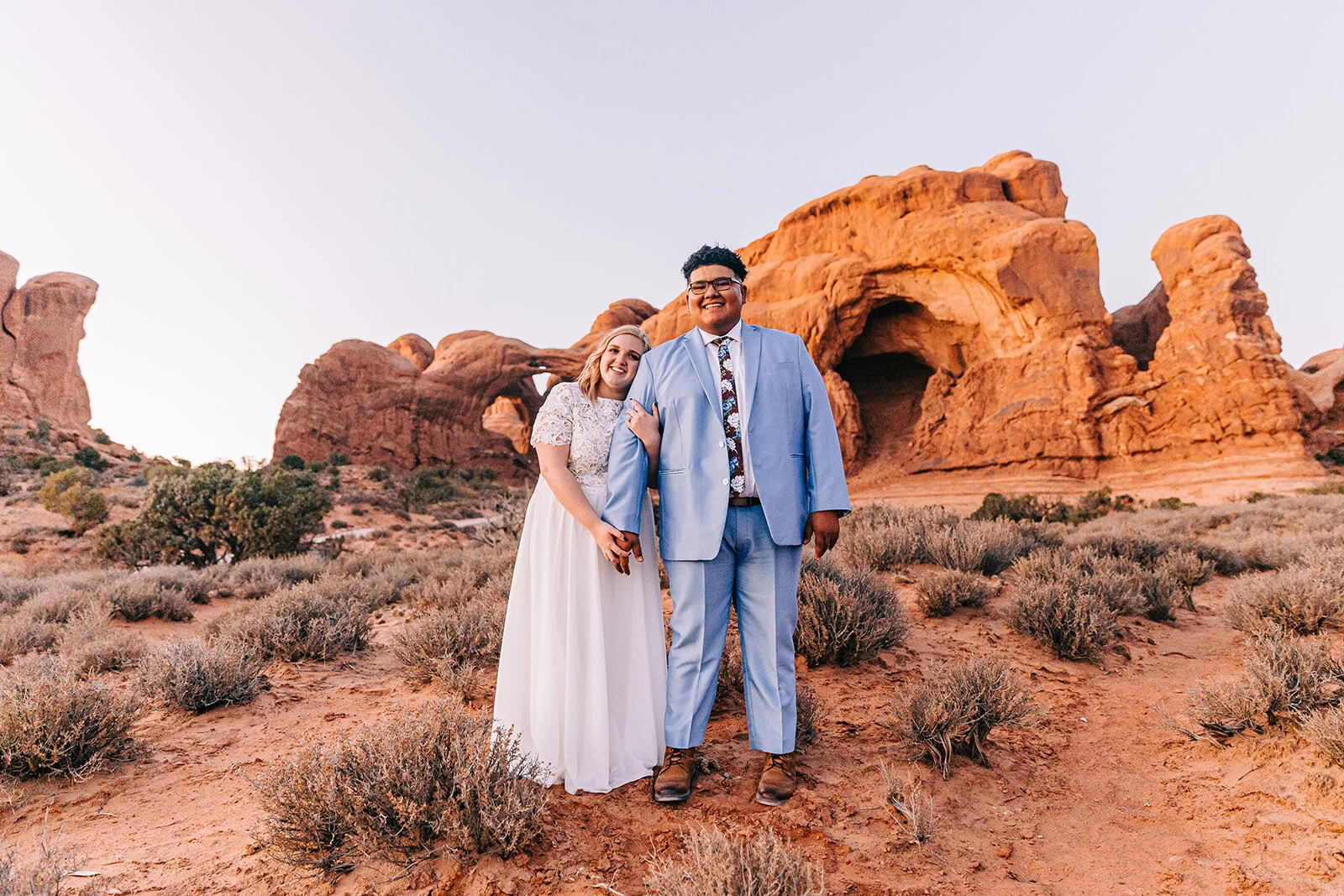 couple cuddling and smiling pose moab utah groom smiling powder blue suit groom fashion modest wedding dress wedding dress inspiration white dress veil bouquet inspo double arch elephant rock professional photographers in utah utah wedding photograp…