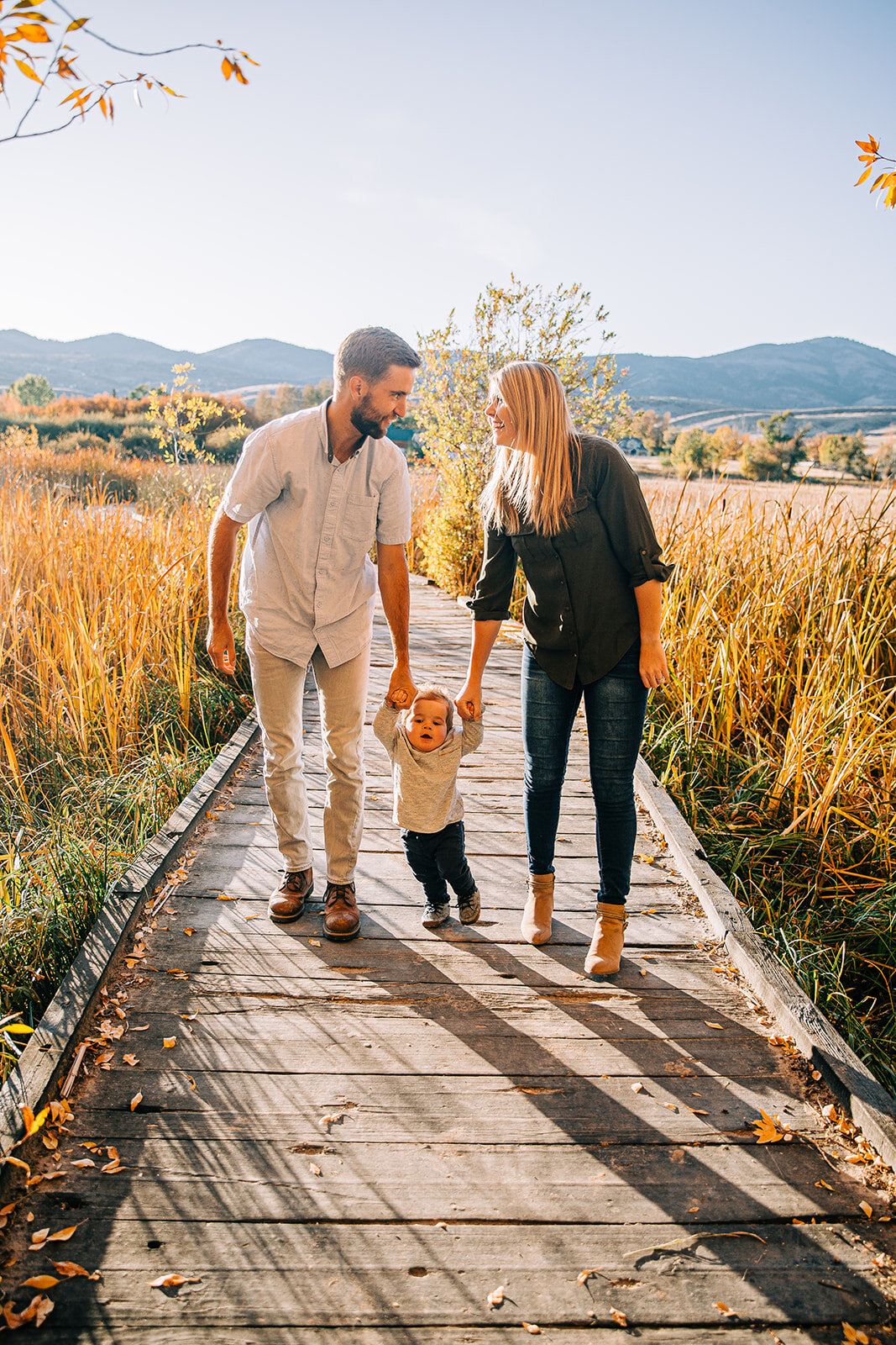  family of three mom and dad helping baby boy stand boardwalk family pictures garden city park bear lake utah together again fields of gold mountains lakeside photos professional photographers in utah utah family photographers extended family sibling
